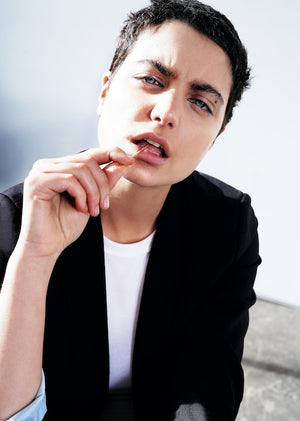 Close up image of model holding toothpick in mouth looking at camera wearing blazer blazer.