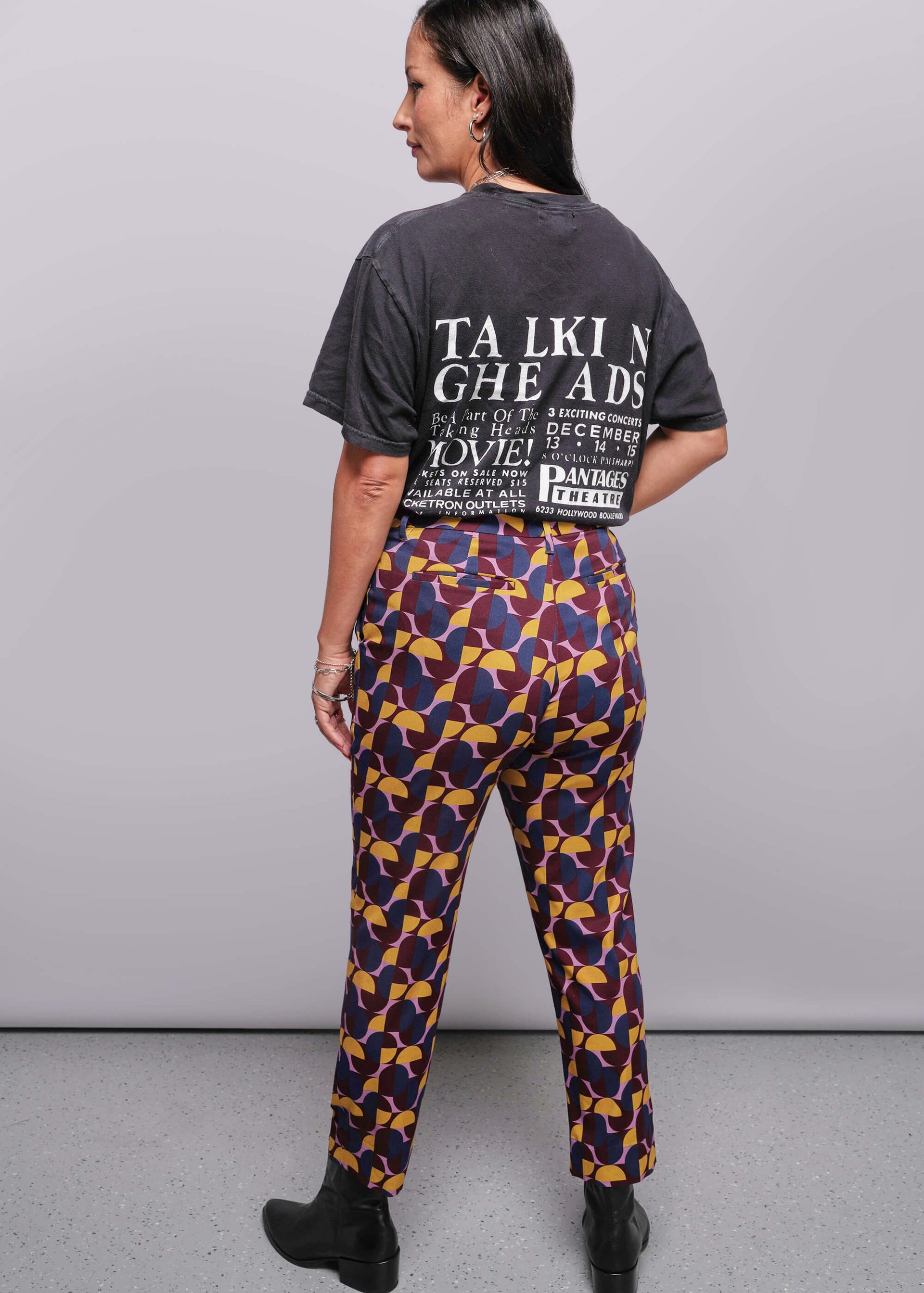 S=Woman wearing a black t-shirt and patterned pants against a gray background