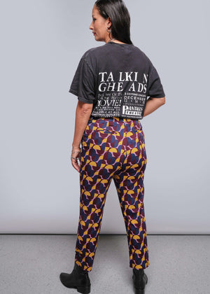 S=Woman wearing a black t-shirt and patterned pants against a gray background