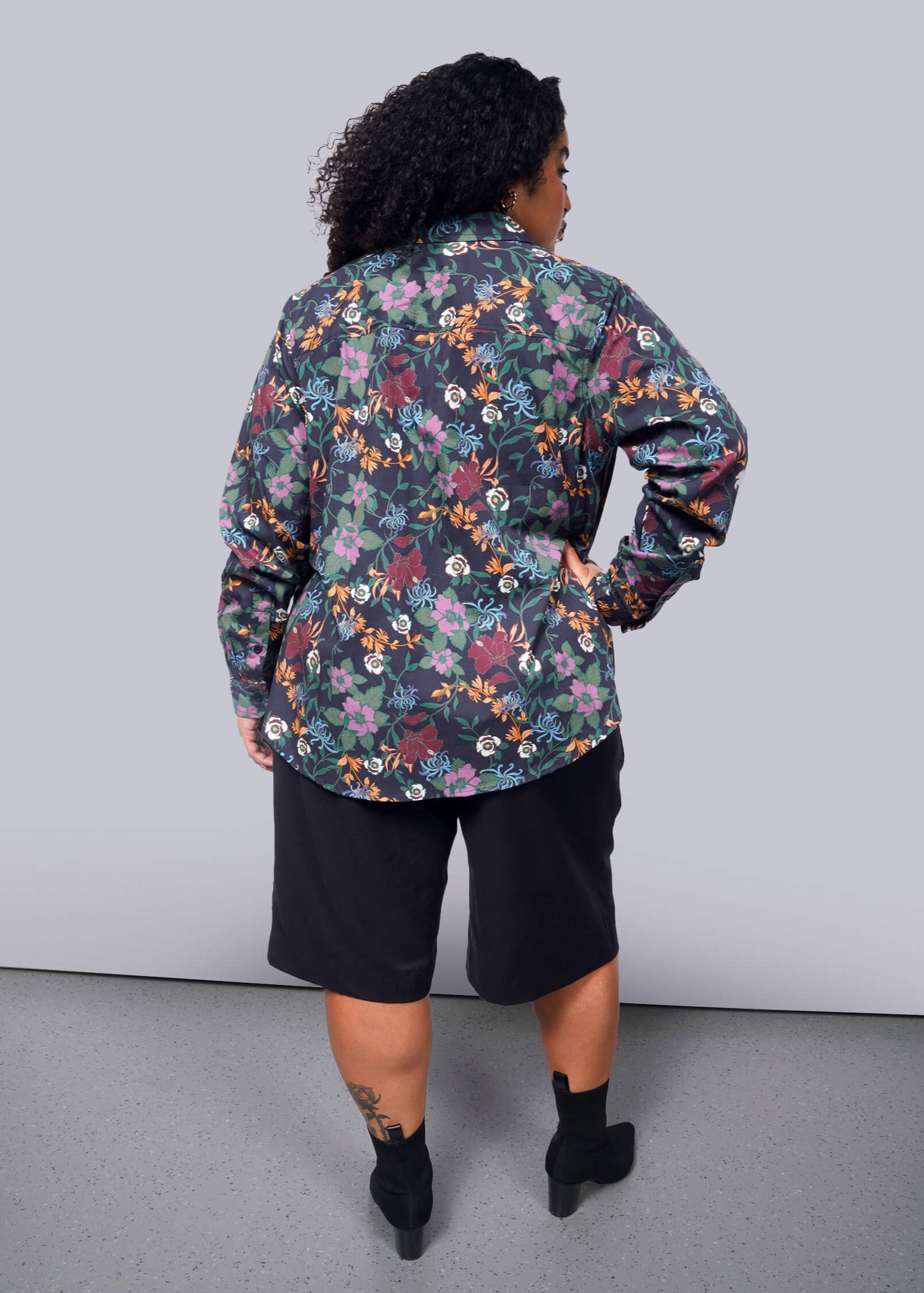 1X=Person wearing a floral shirt and black shorts against a plain background