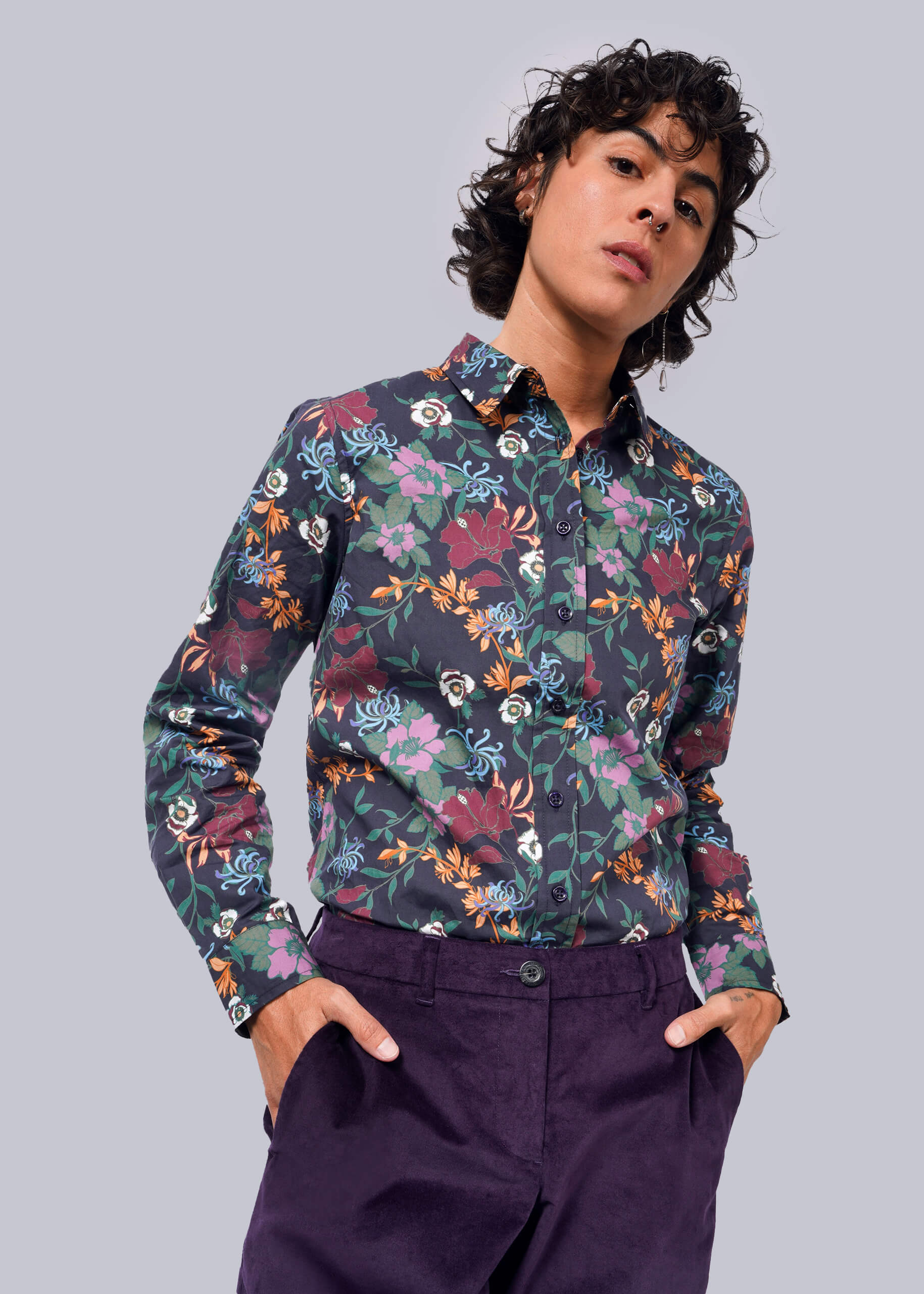 S= A person wearing a long sleeve button-up shirt with a floral pattern and button cuffs. The shirt is primarily navy with multicolored floral accents.