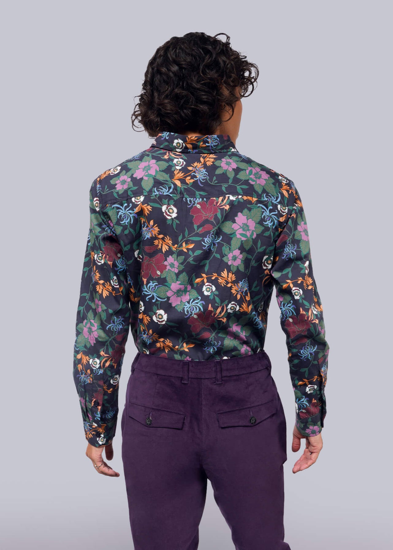 S=Person wearing a floral shirt and purple pants against a plain background