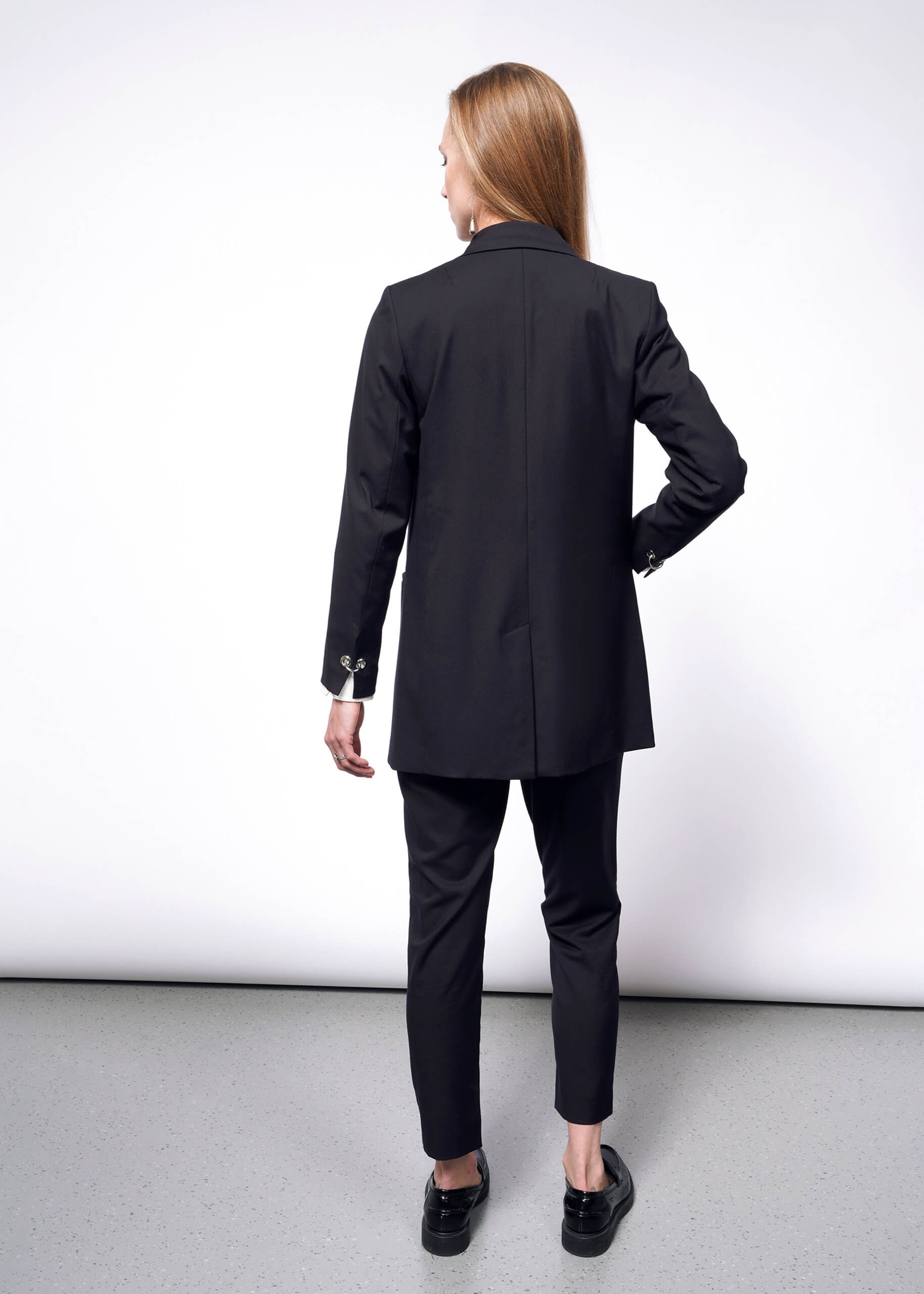 S=A woman with long hair, facing away on a neutral background, wears a Debbie Harry X Wildfang Double Breasted Blazer with matching pants, complemented by black shoes with metal detailing.