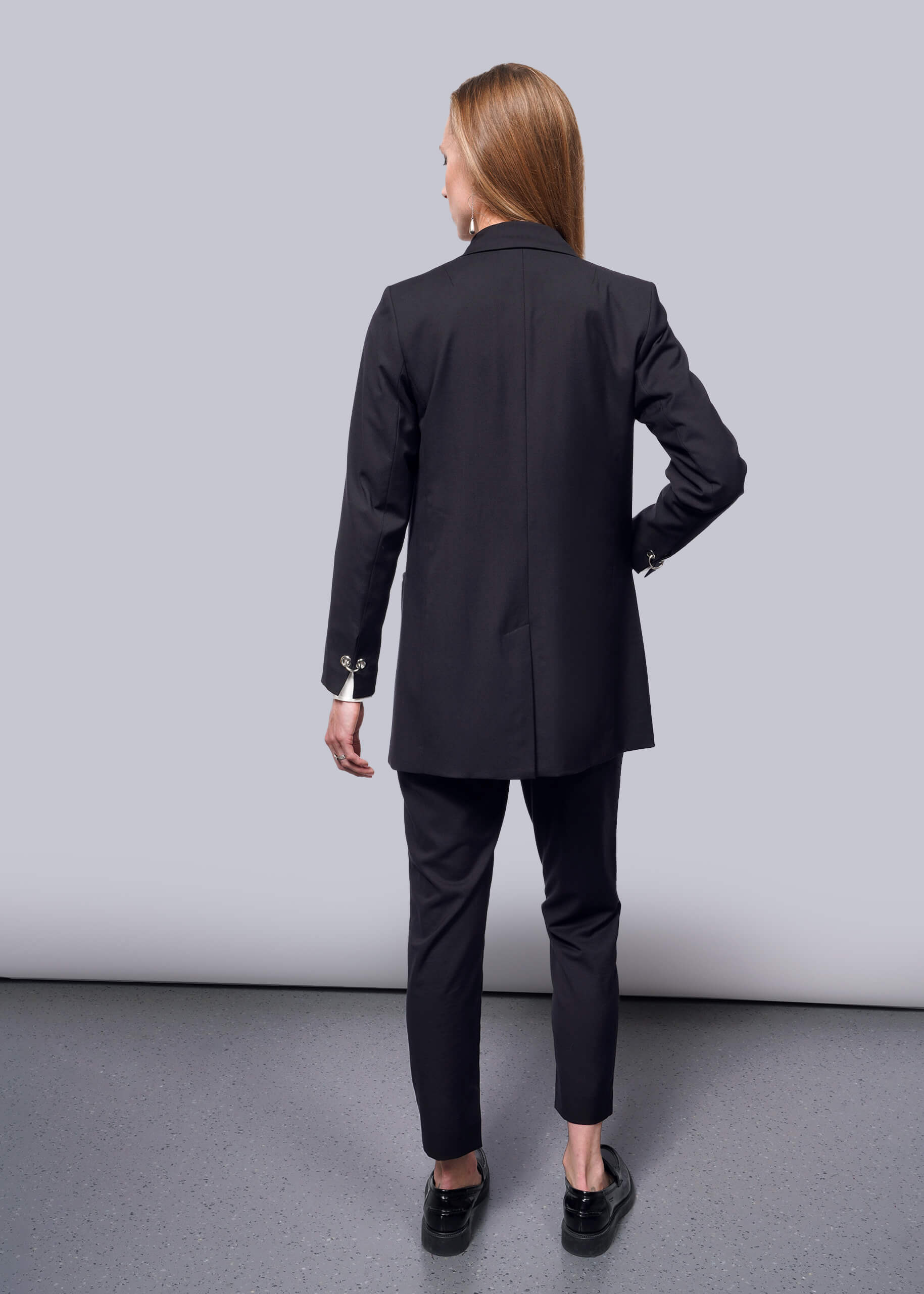 S=A woman with long hair, facing away on a neutral background, wears a Debbie Harry X Wildfang Double Breasted Blazer with matching pants, complemented by black shoes with metal detailing.