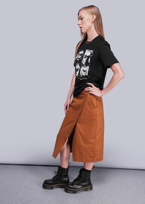 S=Person wearing a black t-shirt with graphic design, brown skirt, and black boots on a plain background