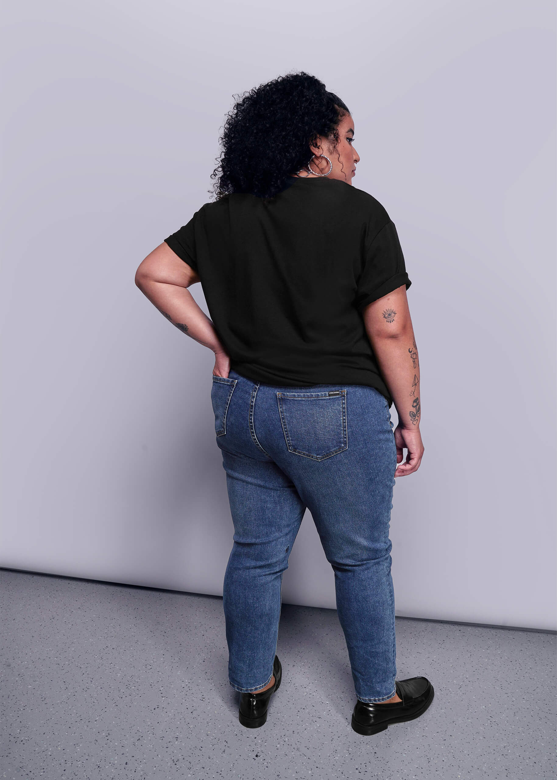 1X=Person wearing a black t-shirt and blue jeans standing against a plain background