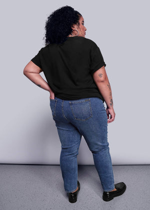 1X=Person wearing a black t-shirt and blue jeans standing against a plain background