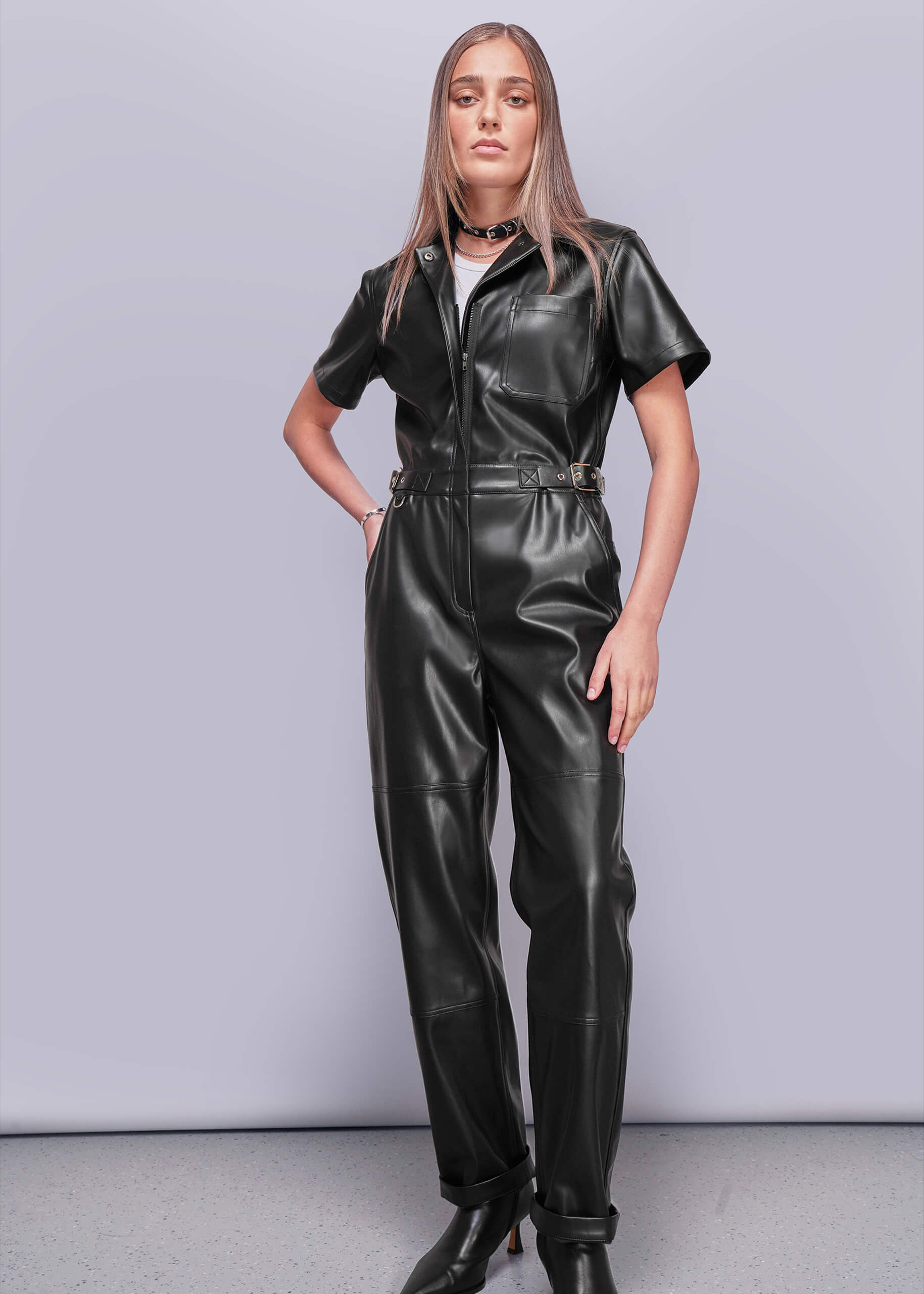 S=Person wearing a black vegan leather jumpsuit against a plain background