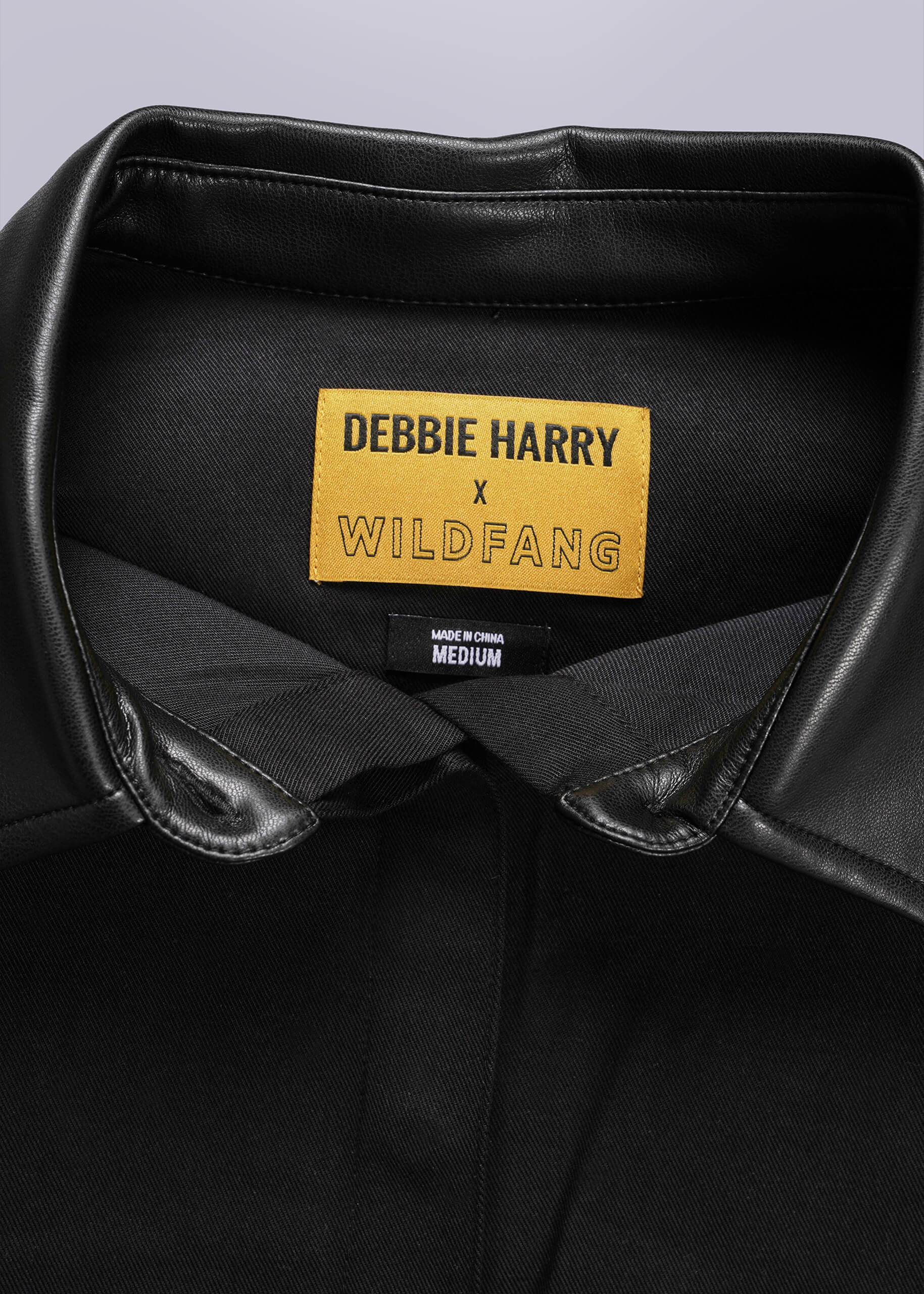 Black leather vest with a yellow label featuring 'Debbie Harry x Wildfang' on a gray background.