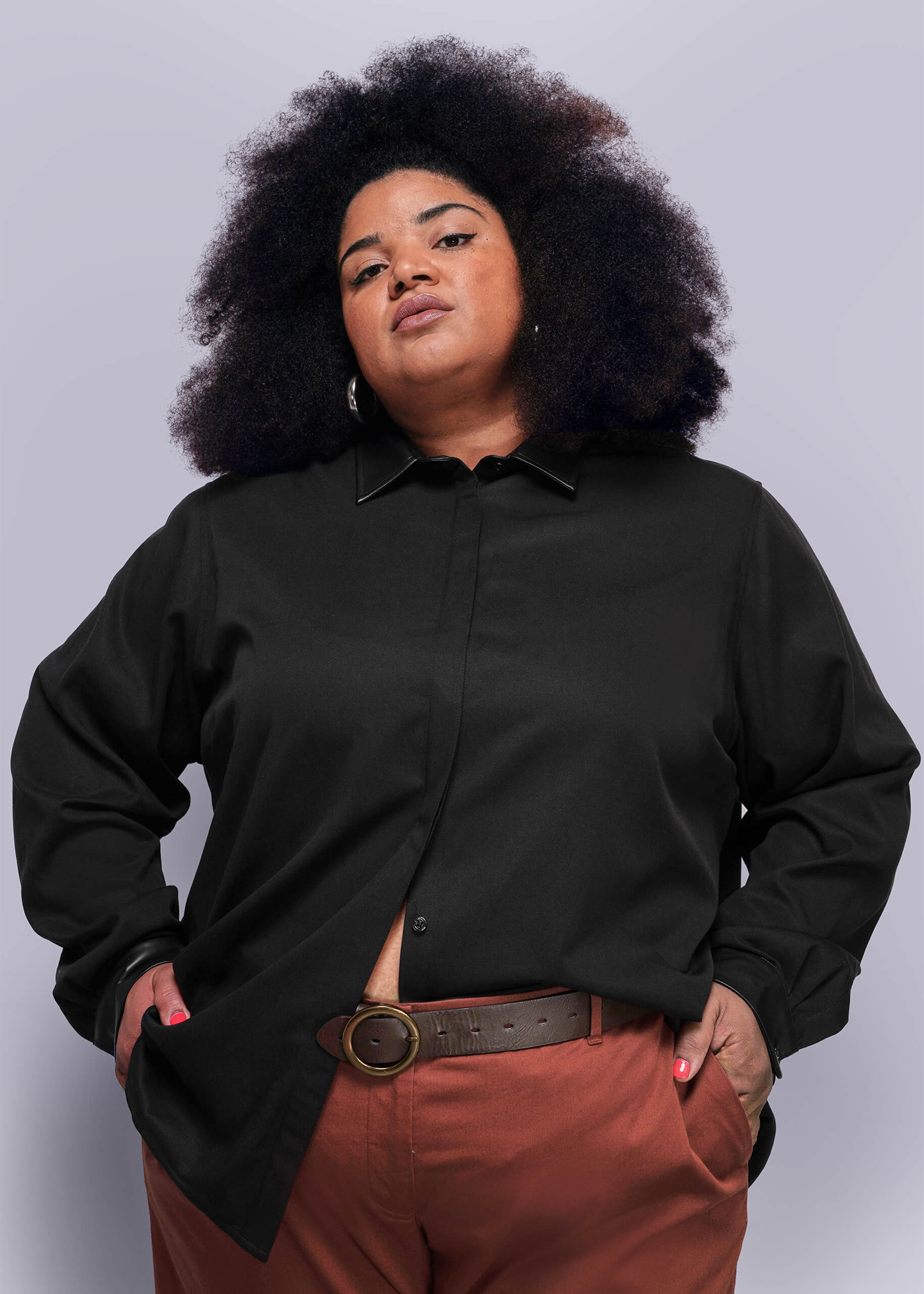 1X=Person wearing a black button up shirt and red pants against a plain background