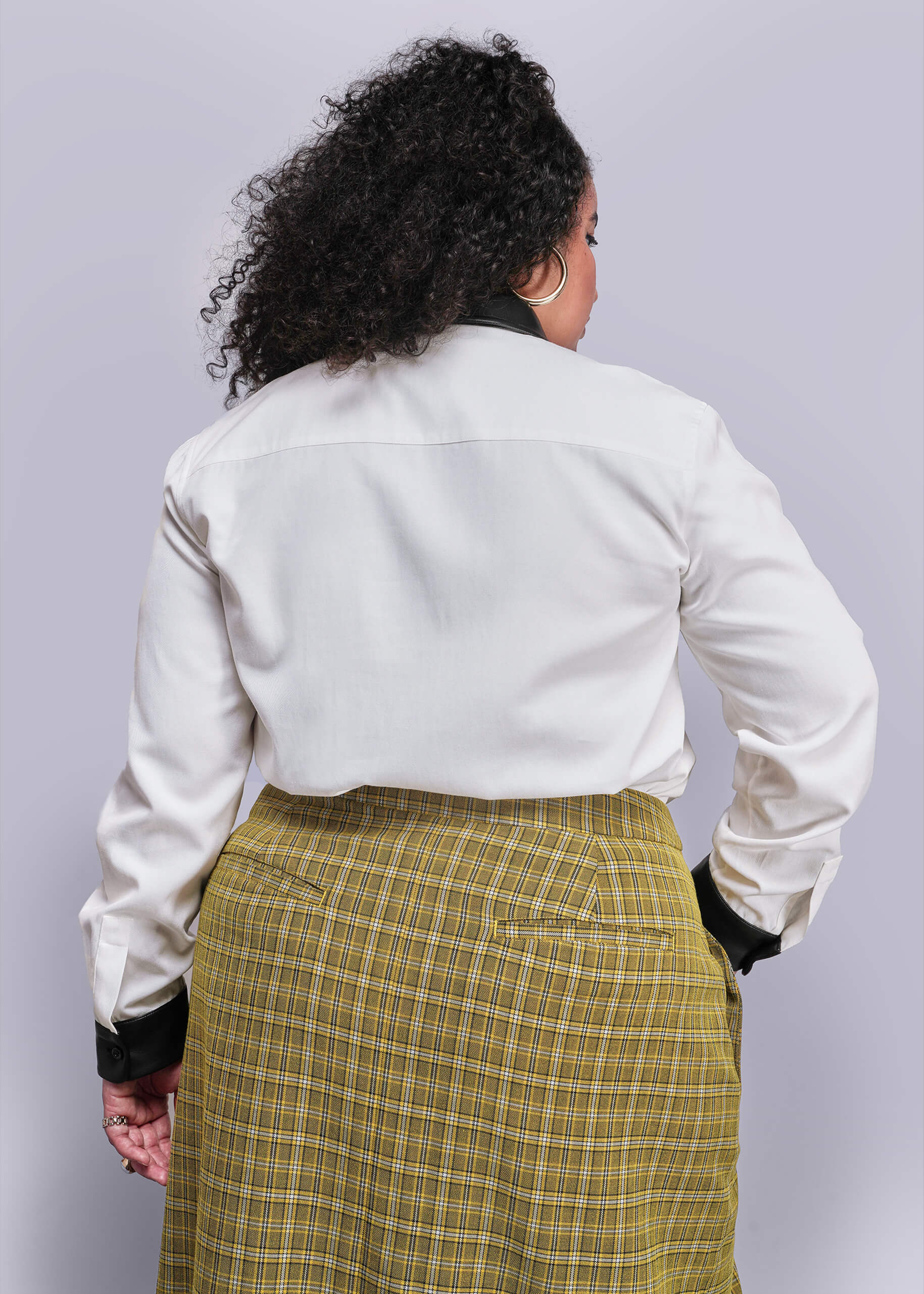 1X=Back view of person wearing a white shirt and yellow plaid skirt against a light gray background