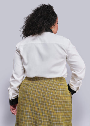 1X=Back view of person wearing a white shirt and yellow plaid skirt against a light gray background