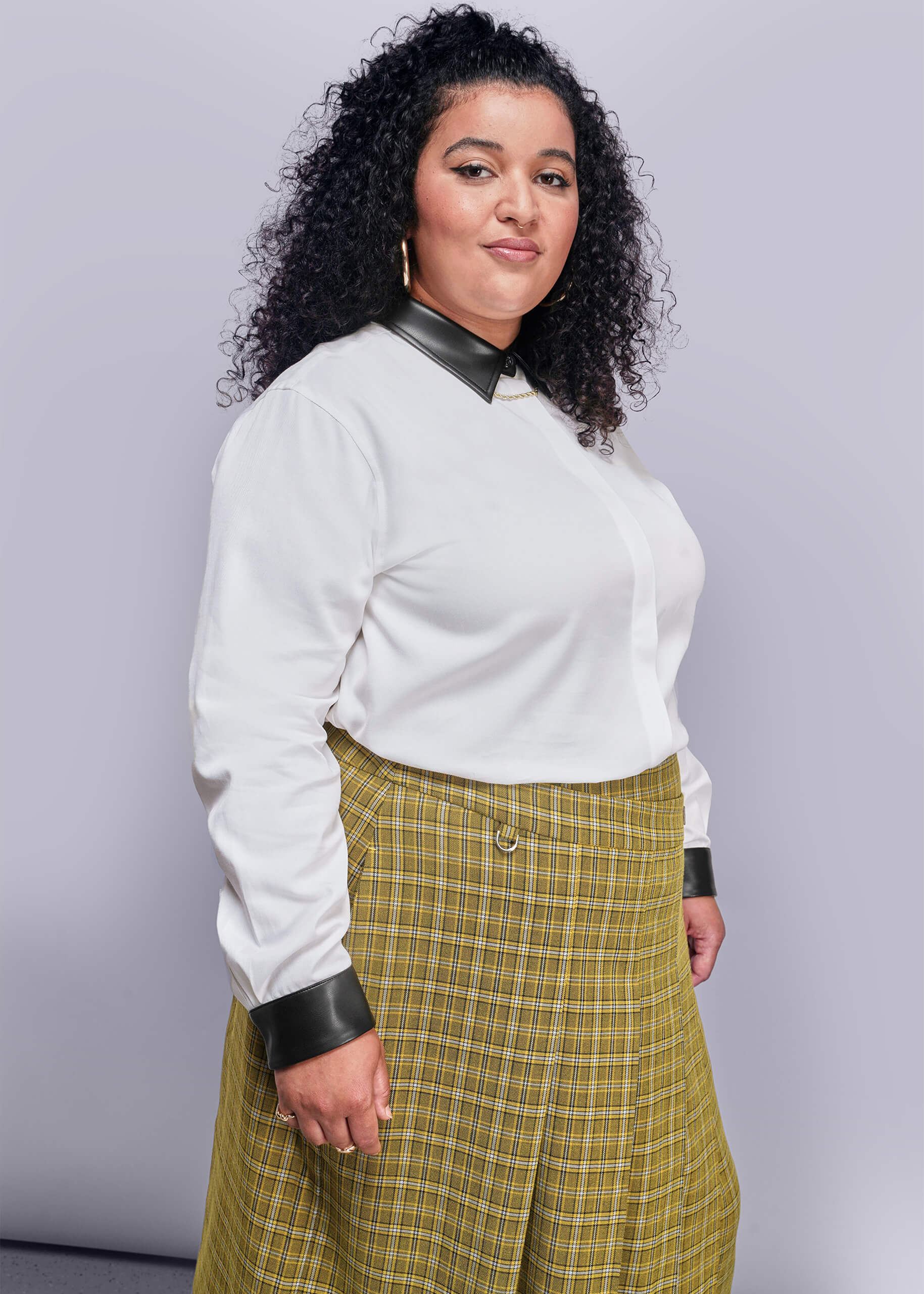 1X=Person wearing a white blouse with black collar and cuffs, and a yellow plaid skirt against a gray background