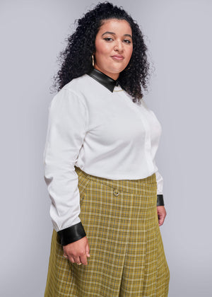 1X=Person wearing a white blouse with black collar and cuffs, and a yellow plaid skirt against a gray background