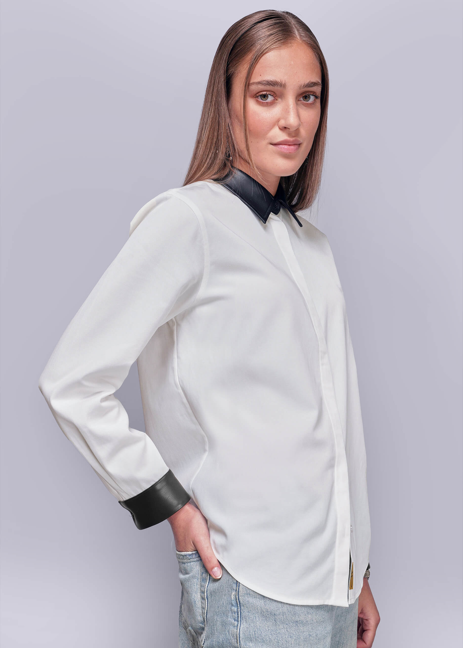 S=Side view of person wearing a white blouse with black vegan leather accents on a plain background