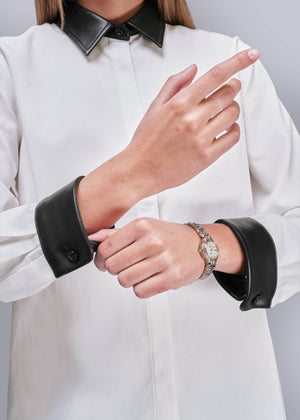 S=Person wearing a white shirt with black vegan leather cuffs and collar, adjusting their sleeve.