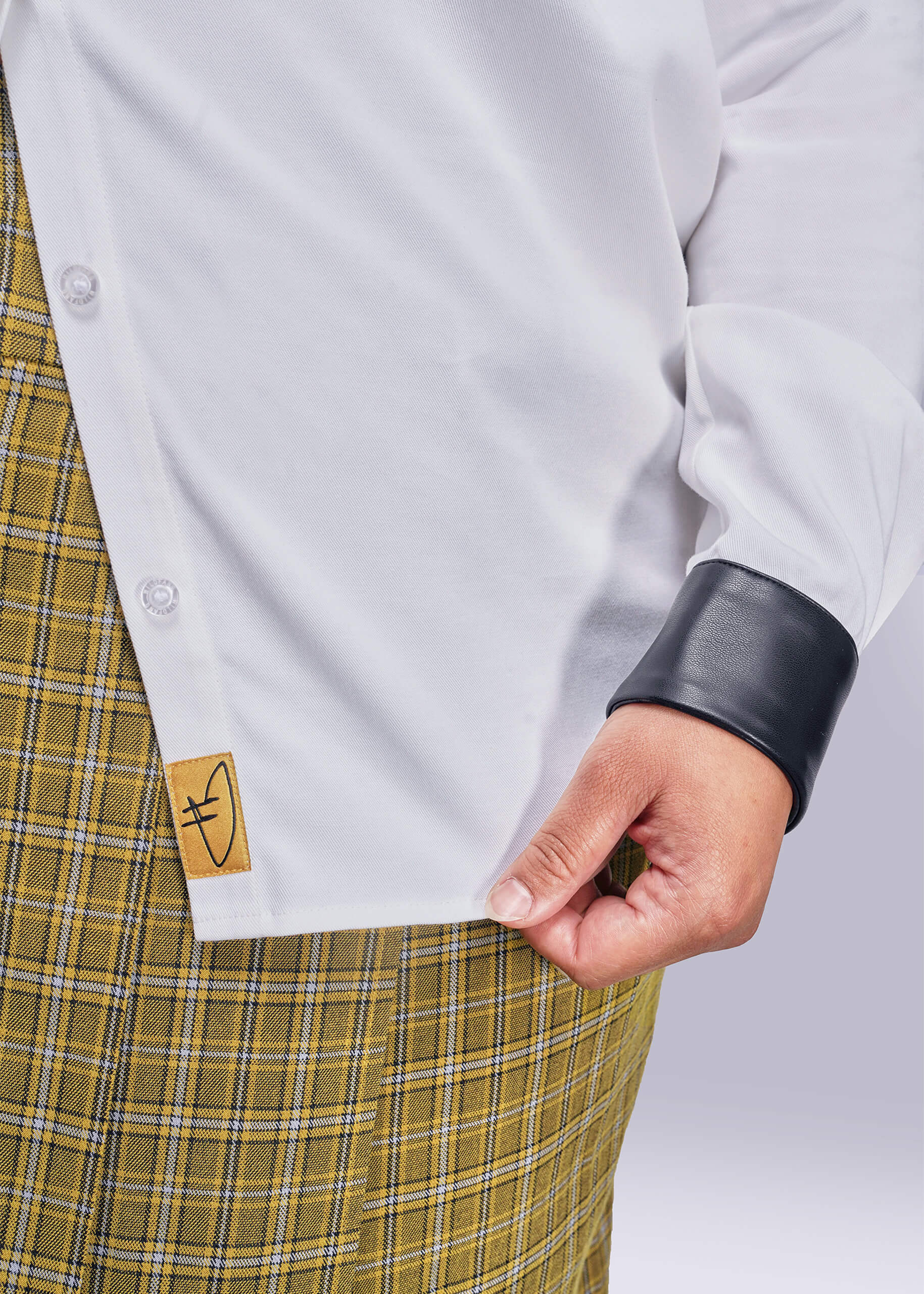 1X=Close-up of a person wearing a white shirt with a black vegan leather cuff and yellow plaid skirt.