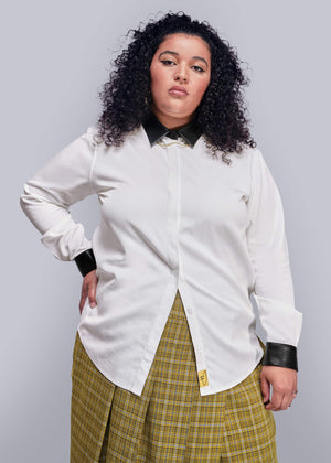 1X=Person wearing a white shirt with black vegan leather cuffs and a yellow plaid skirt on a light gray background