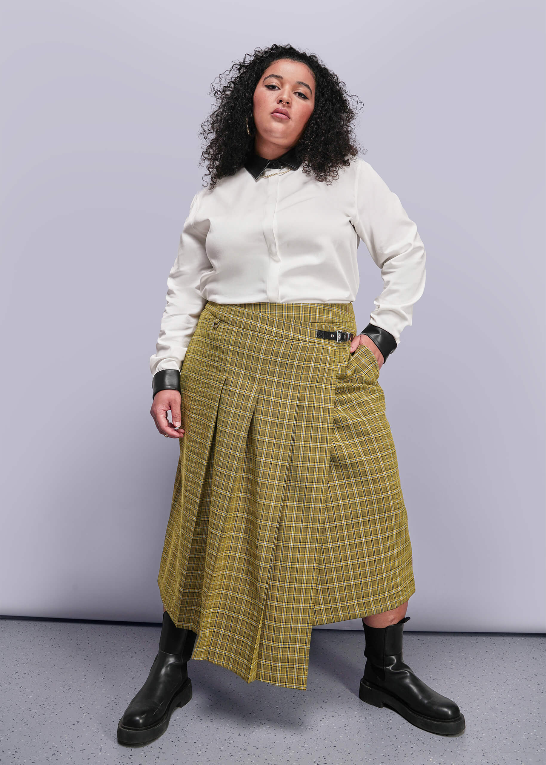 1X=Person wearing a white shirt and yellow plaid skirt against a gray background