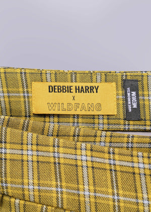Close-up of a yellow label on plaid fabric with 'Debbie Harry x Wildfang' text.