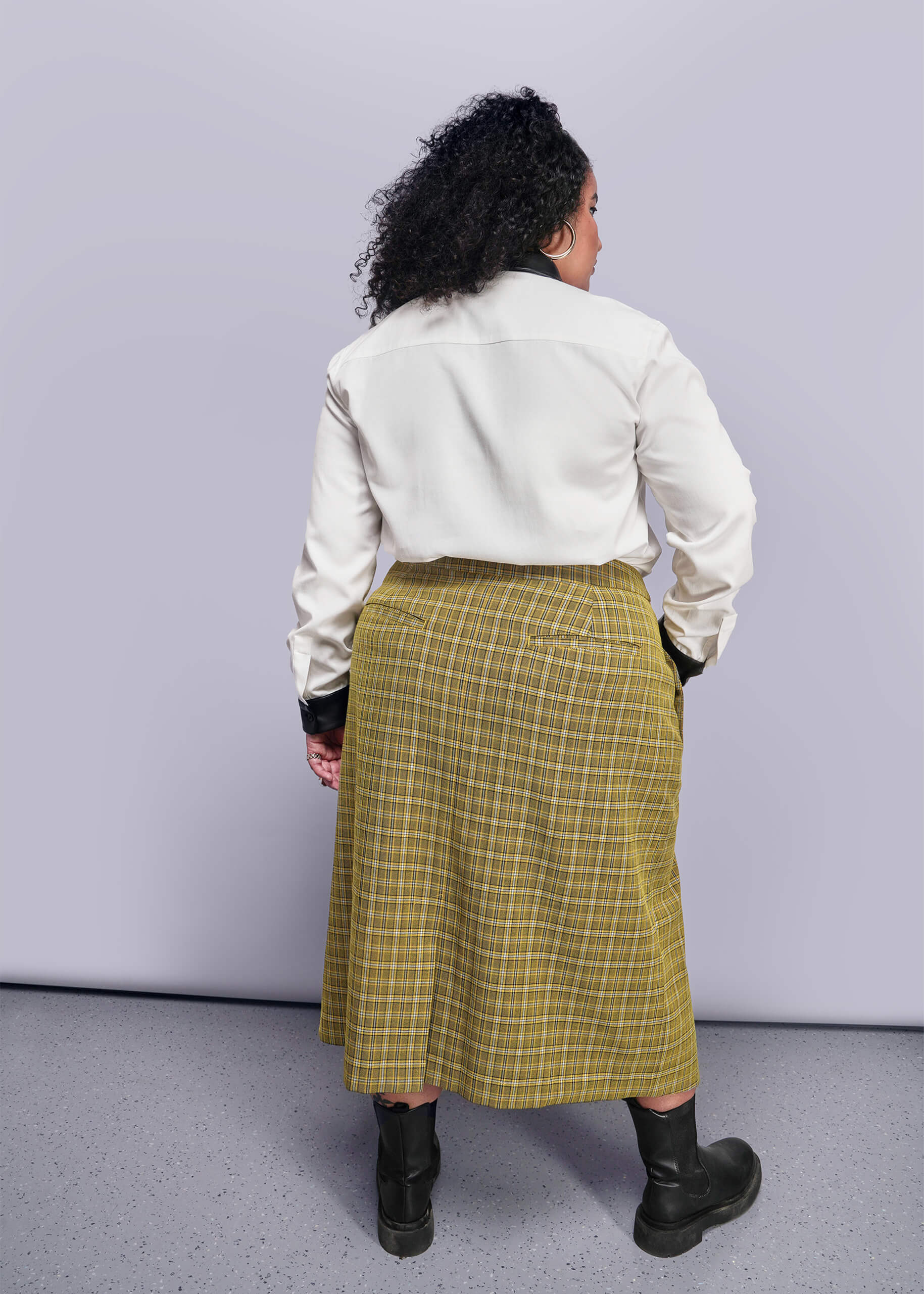 1X=Back view of person wearing a white shirt and yellow plaid skirt against a plain background