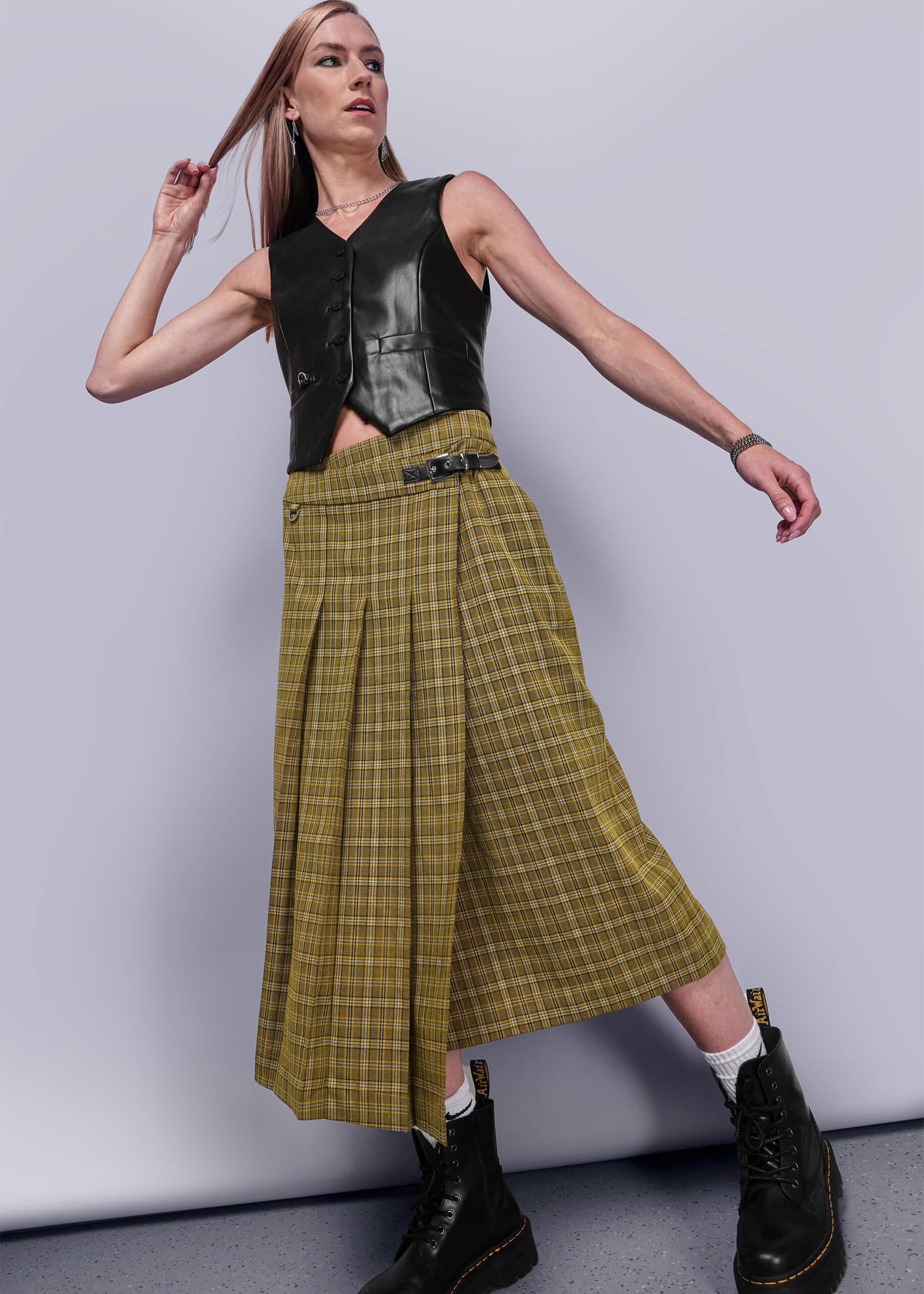 S=Person wearing a yellow plaid skirt and black leather vest against a plain background