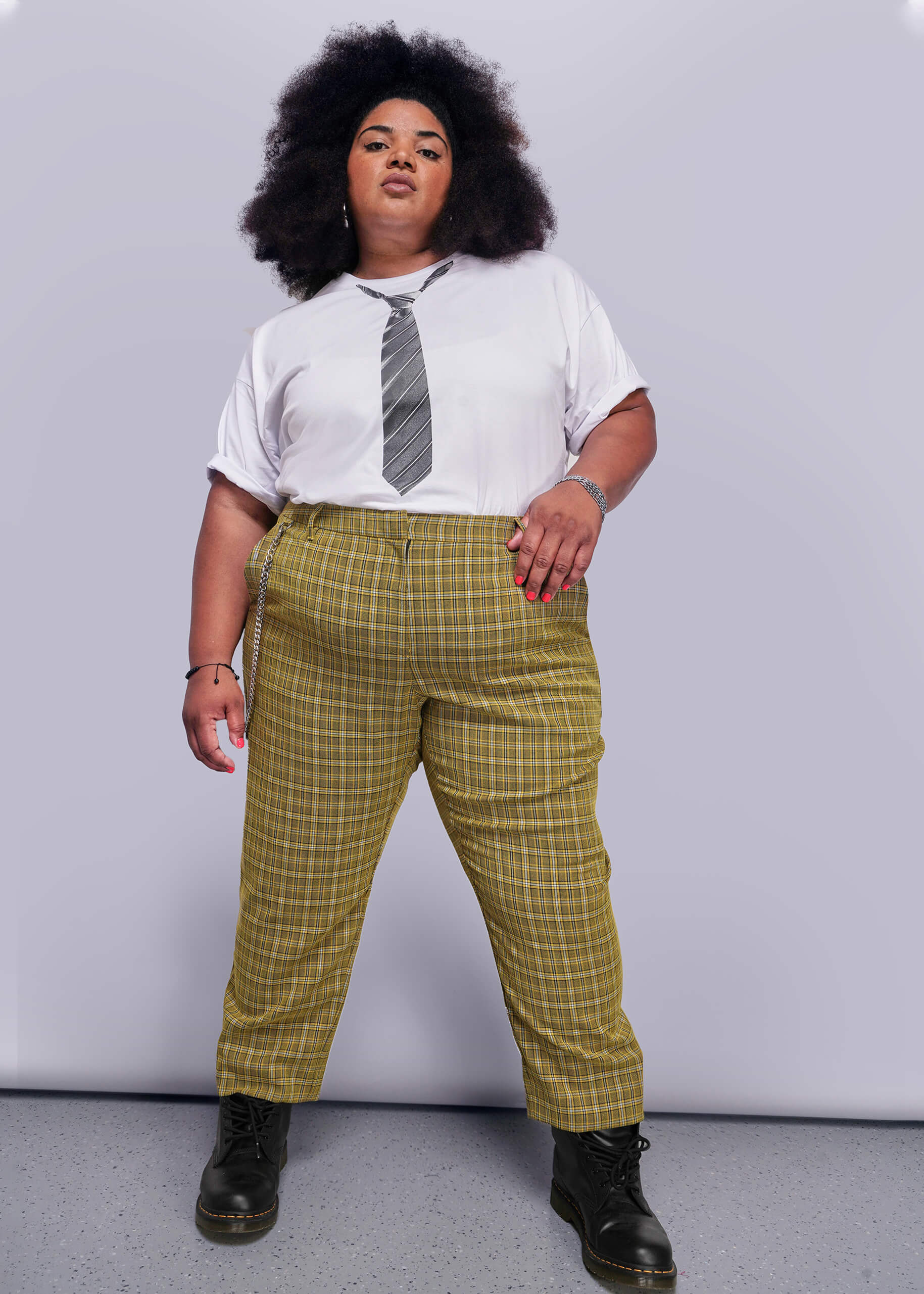 1X=Person wearing a white shirt with a tie graphic, yellow plaid pants, and black shoes on a plain background