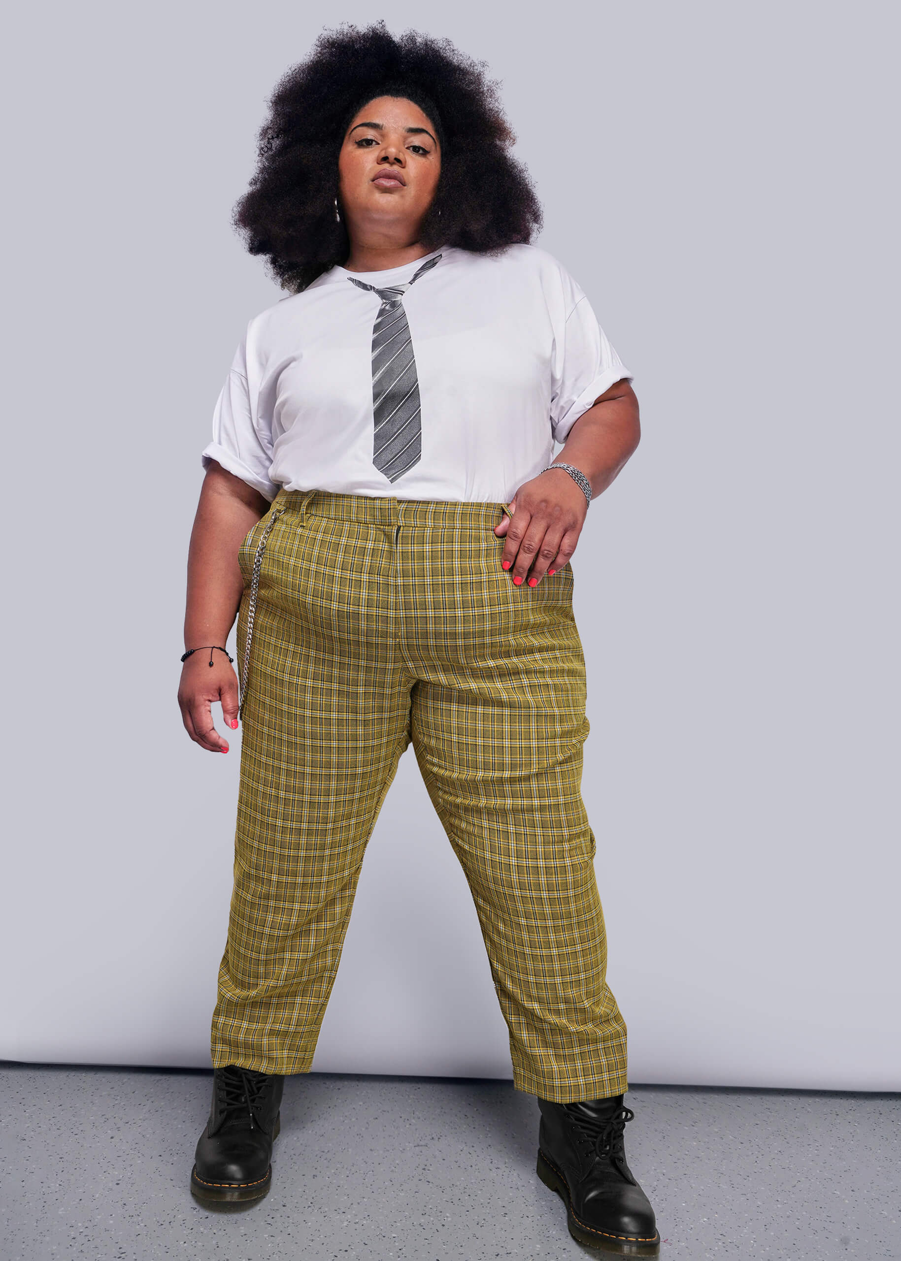 1X=Person wearing a white shirt with a tie graphic, yellow plaid pants, and black shoes on a plain background