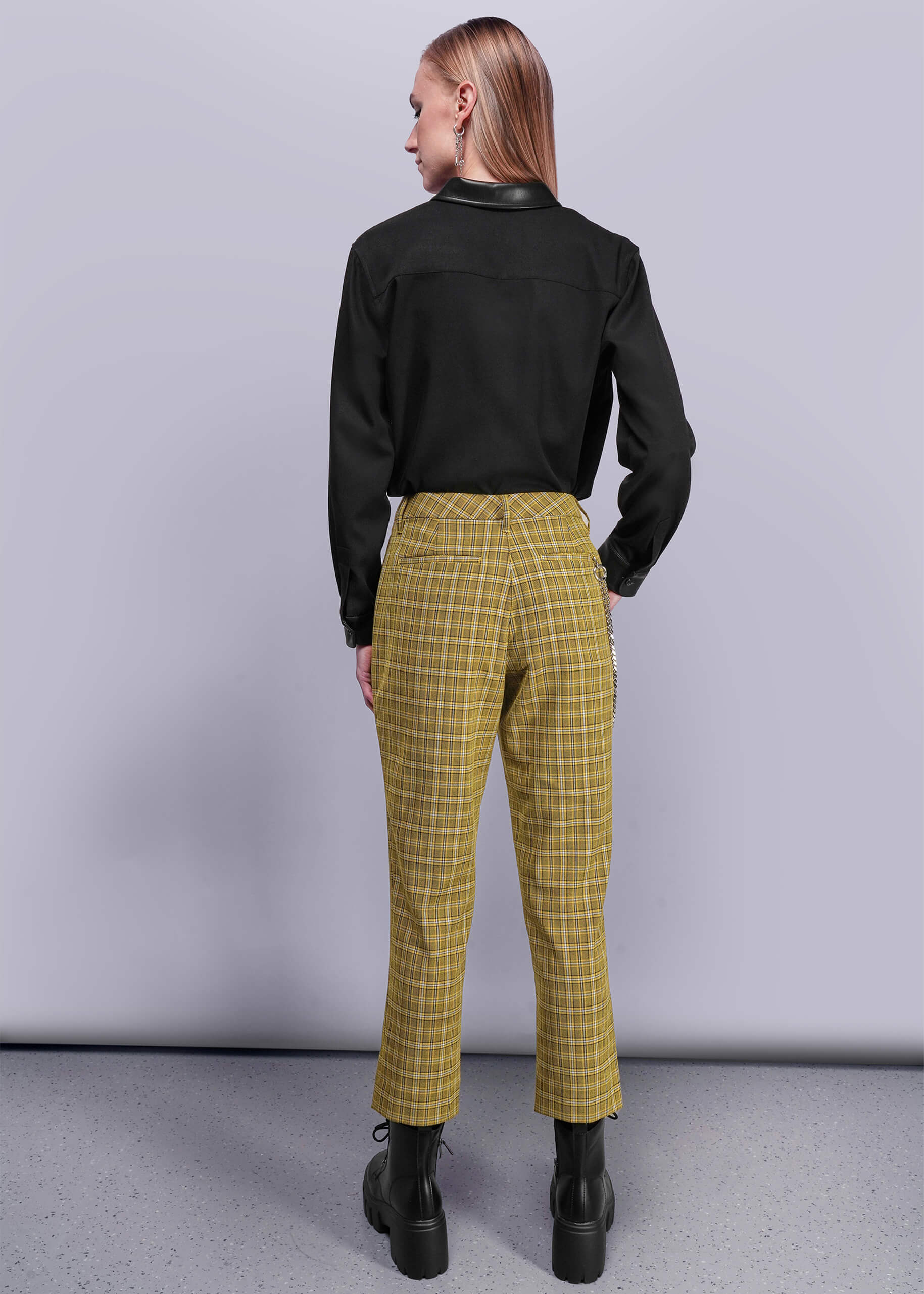 S=Back view of person wearing a black shirt and yellow plaid pants against a plain background
