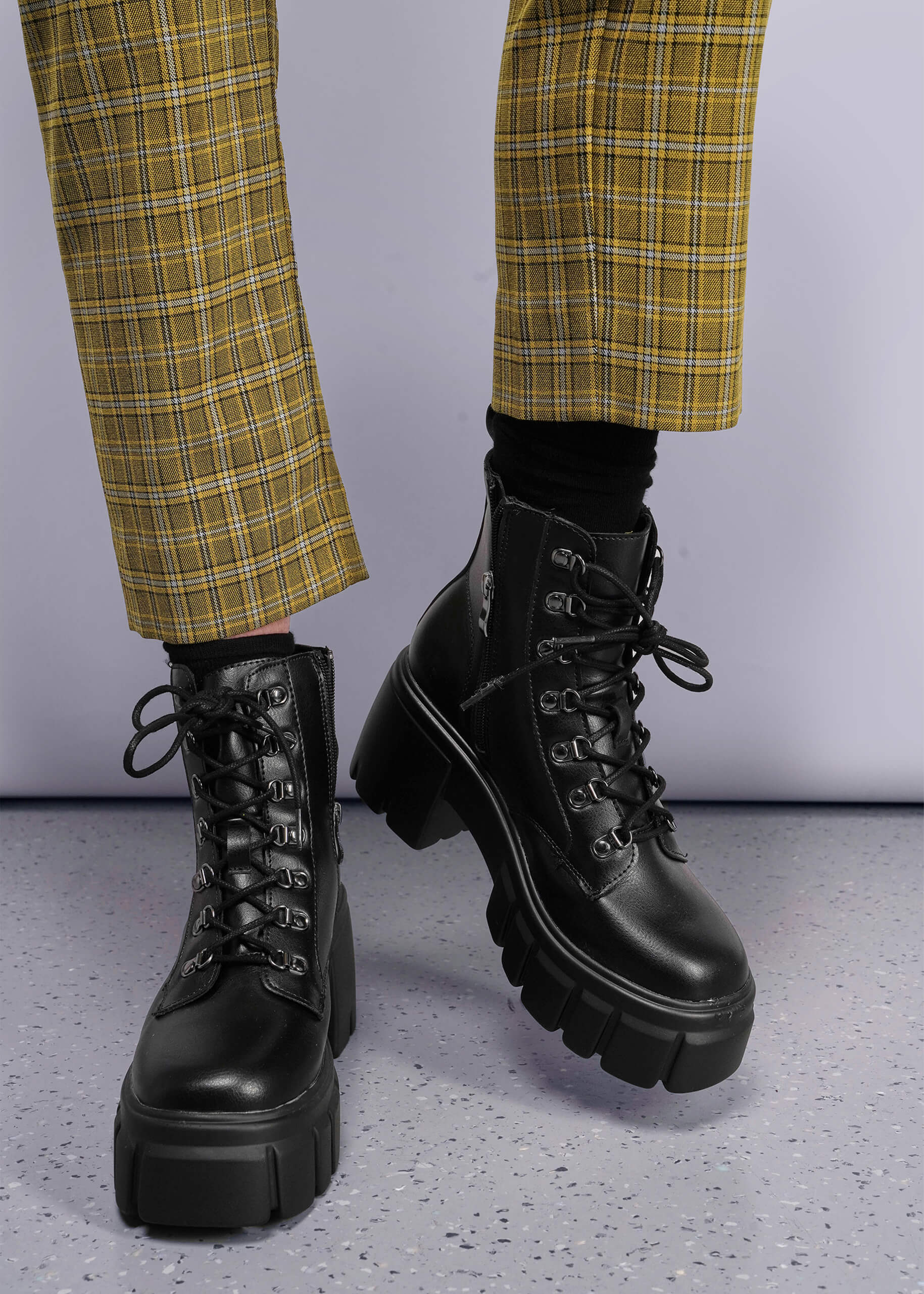 S=Black combat boots worn with yellow plaid pants on a gray floor.