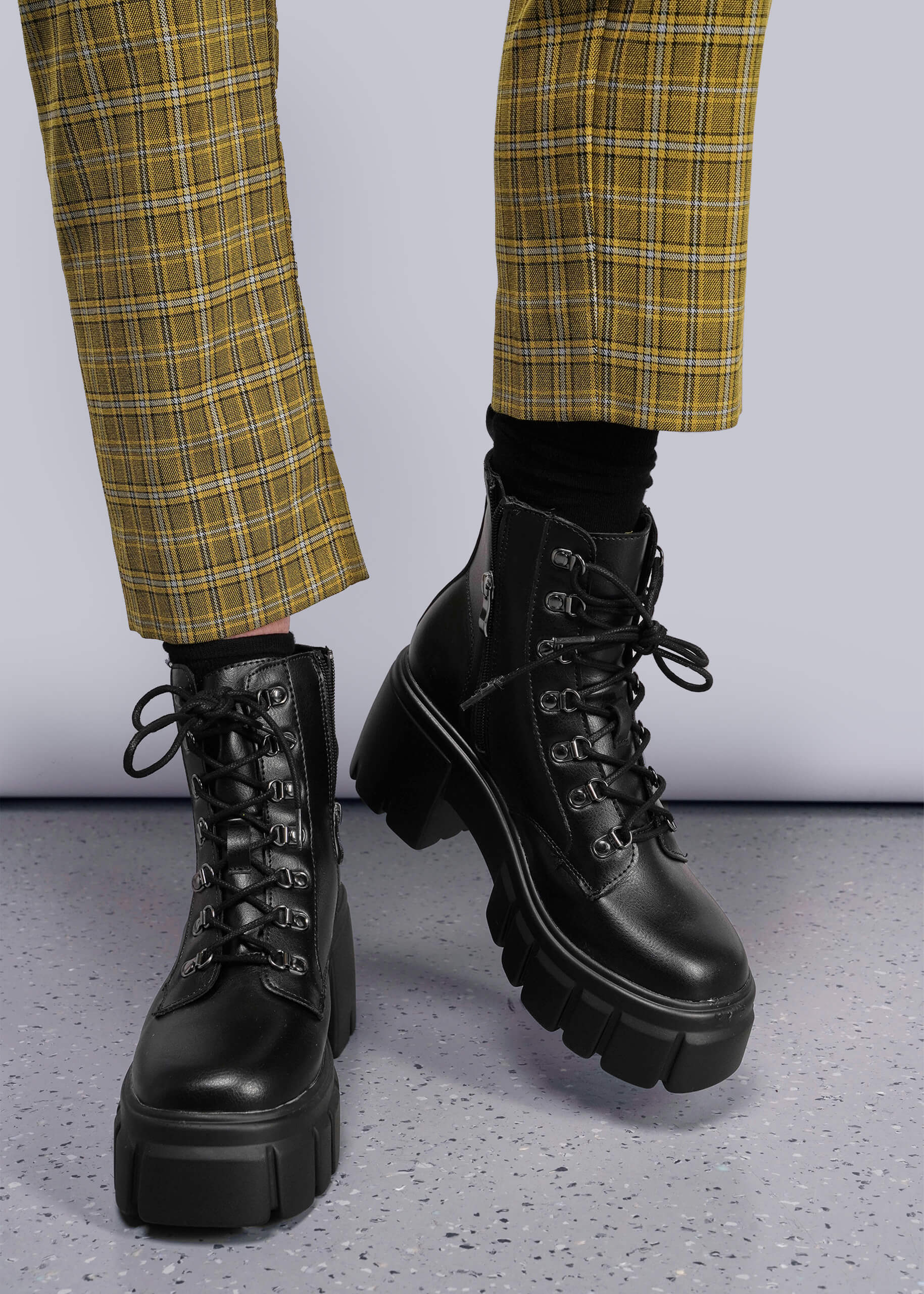 S=Black combat boots worn with yellow plaid pants on a gray floor.