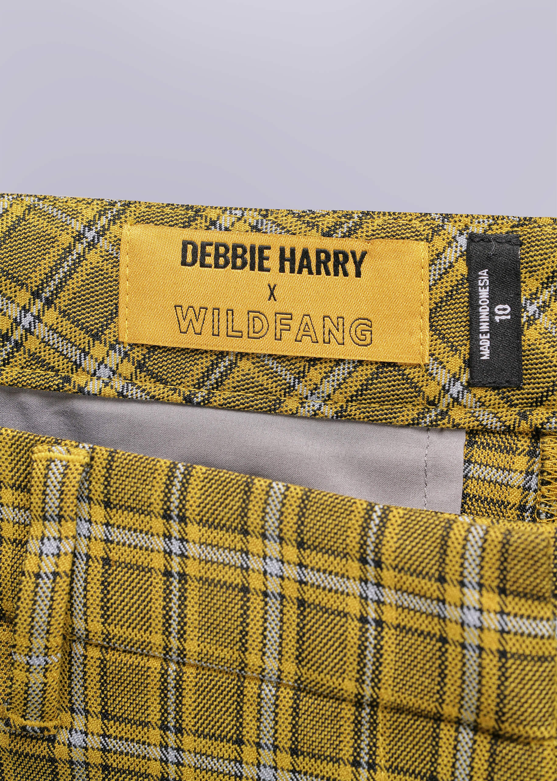 Close-up of yellow plaid pants with a label reading 'Debbie Harry x Wildfang' on a gray background.