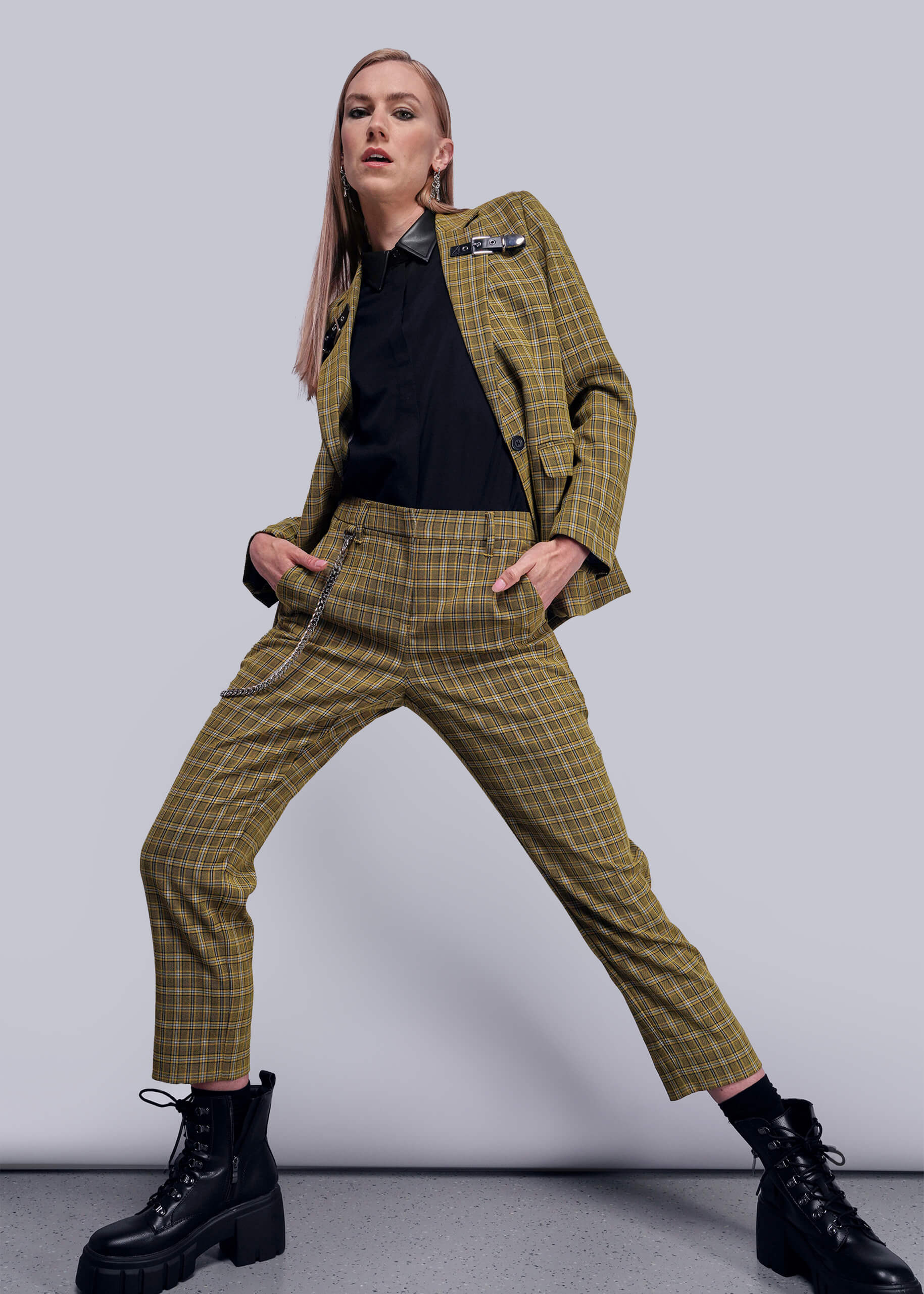 S=Person wearing a yellow plaid suit with black boots on a gray background