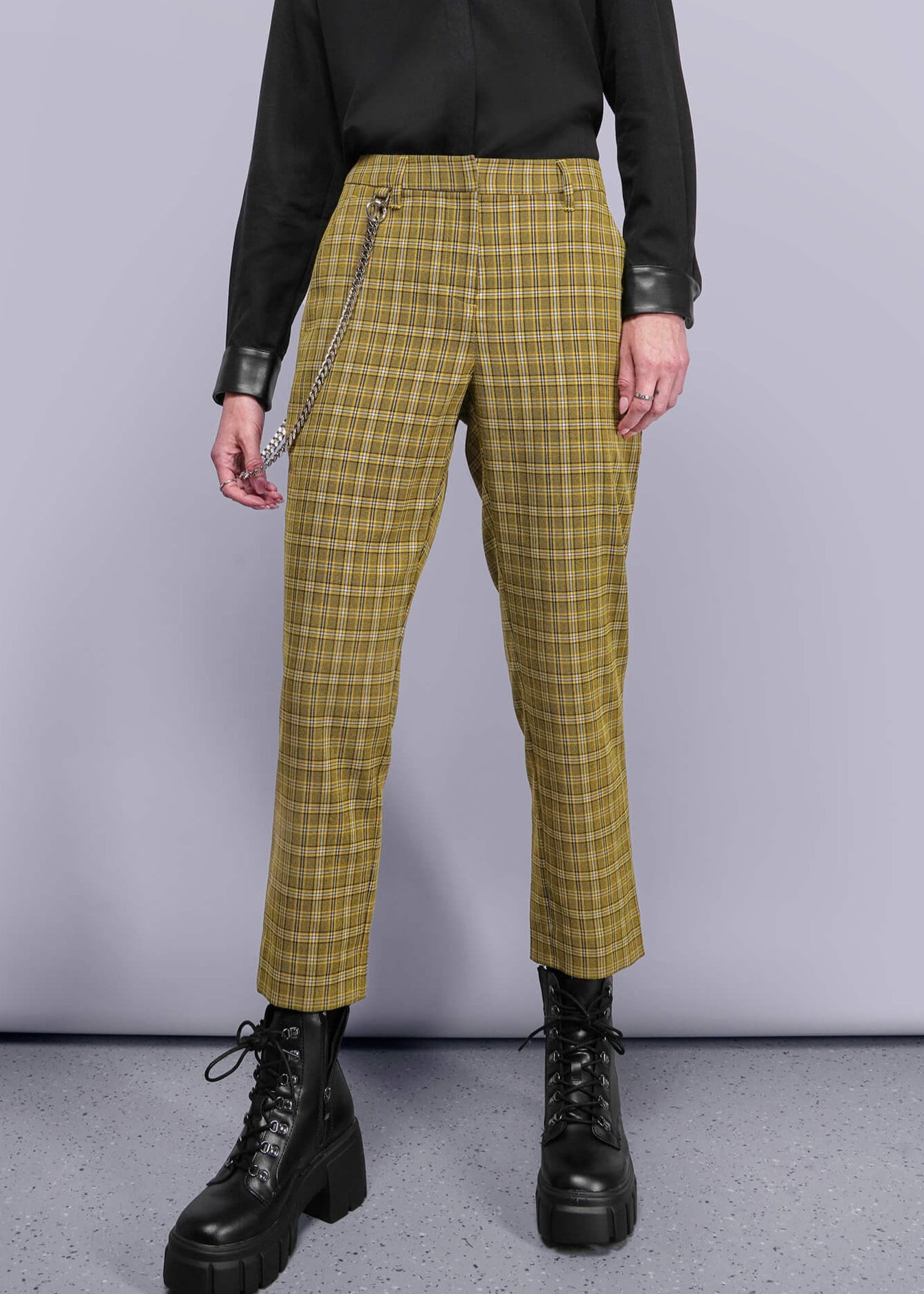 S=Person wearing a black button up shirt and yellow plaid pants against a gray background