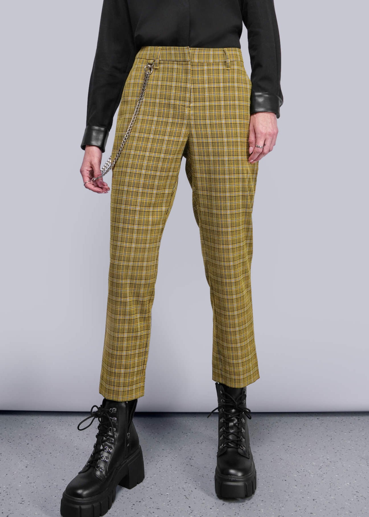 S=Person wearing a black button up shirt and yellow plaid pants against a gray background