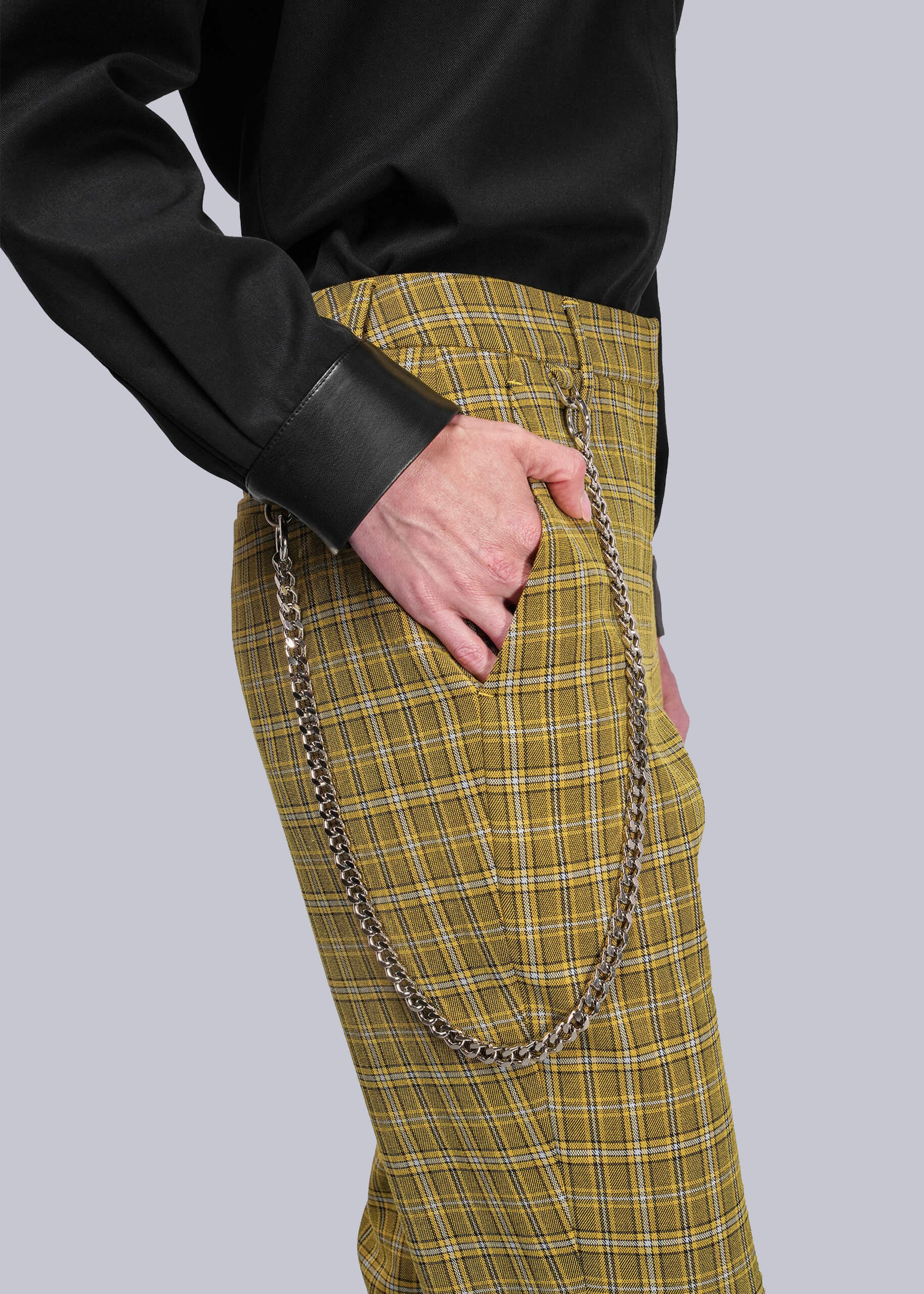 S=Person wearing yellow plaid pants with a black button up on a light gray background