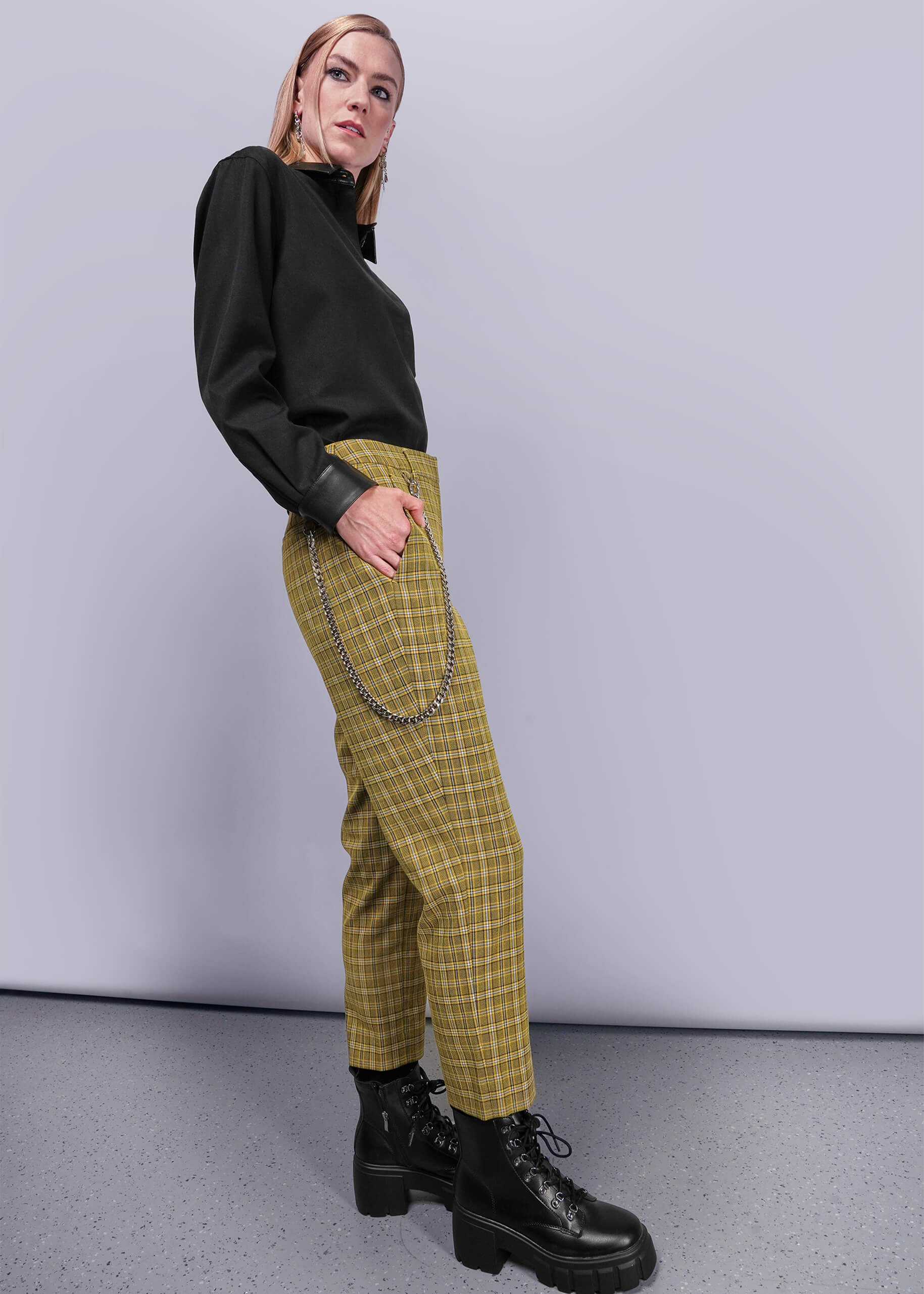 S=Side view of person wearing a black top and yellow plaid pants with chains, standing against a plain background.