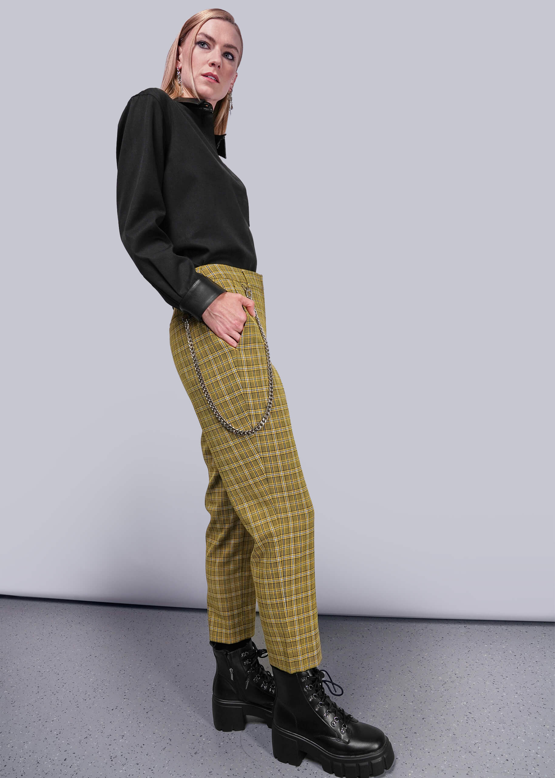 S=Side view of person wearing a black top and yellow plaid pants with chains, standing against a plain background.
