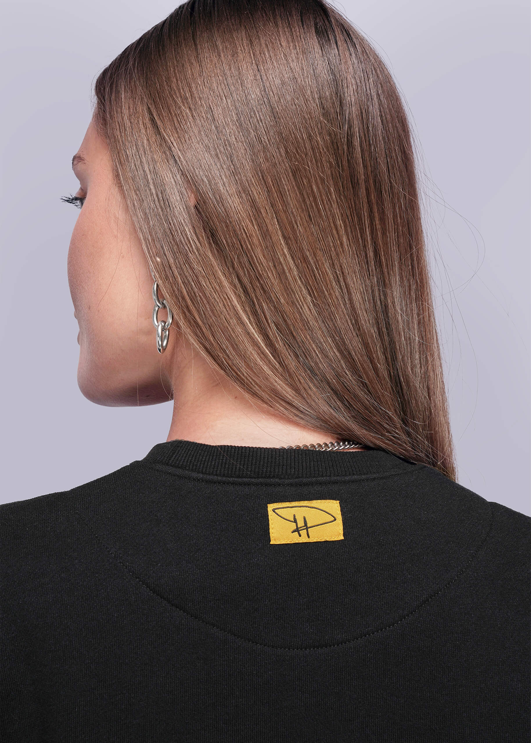 S=Close up of back of person wearing a black sweatshirt with a yellow logo on a plain background