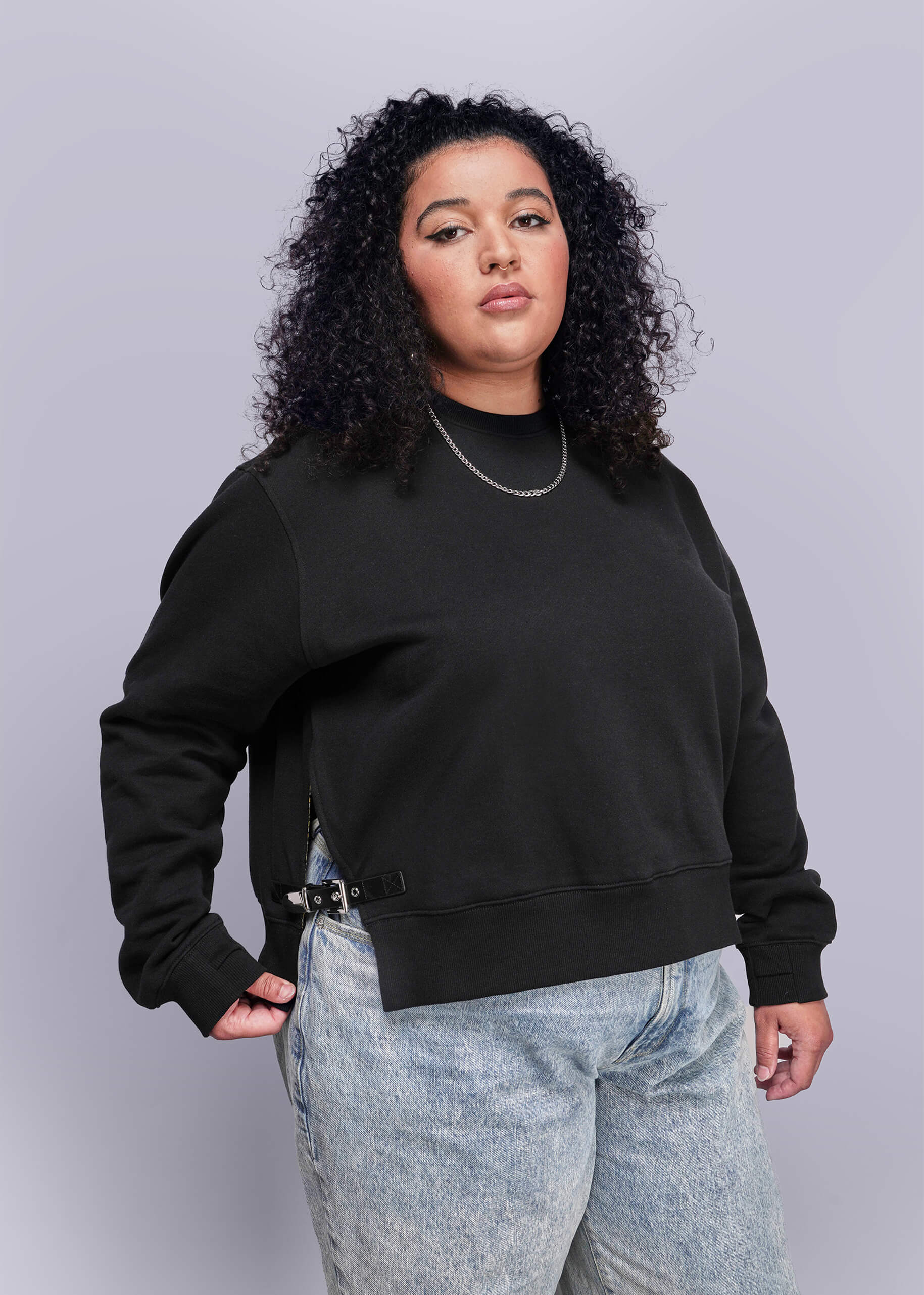 1X=Person wearing a black sweatshirt and light blue jeans against a gray background
