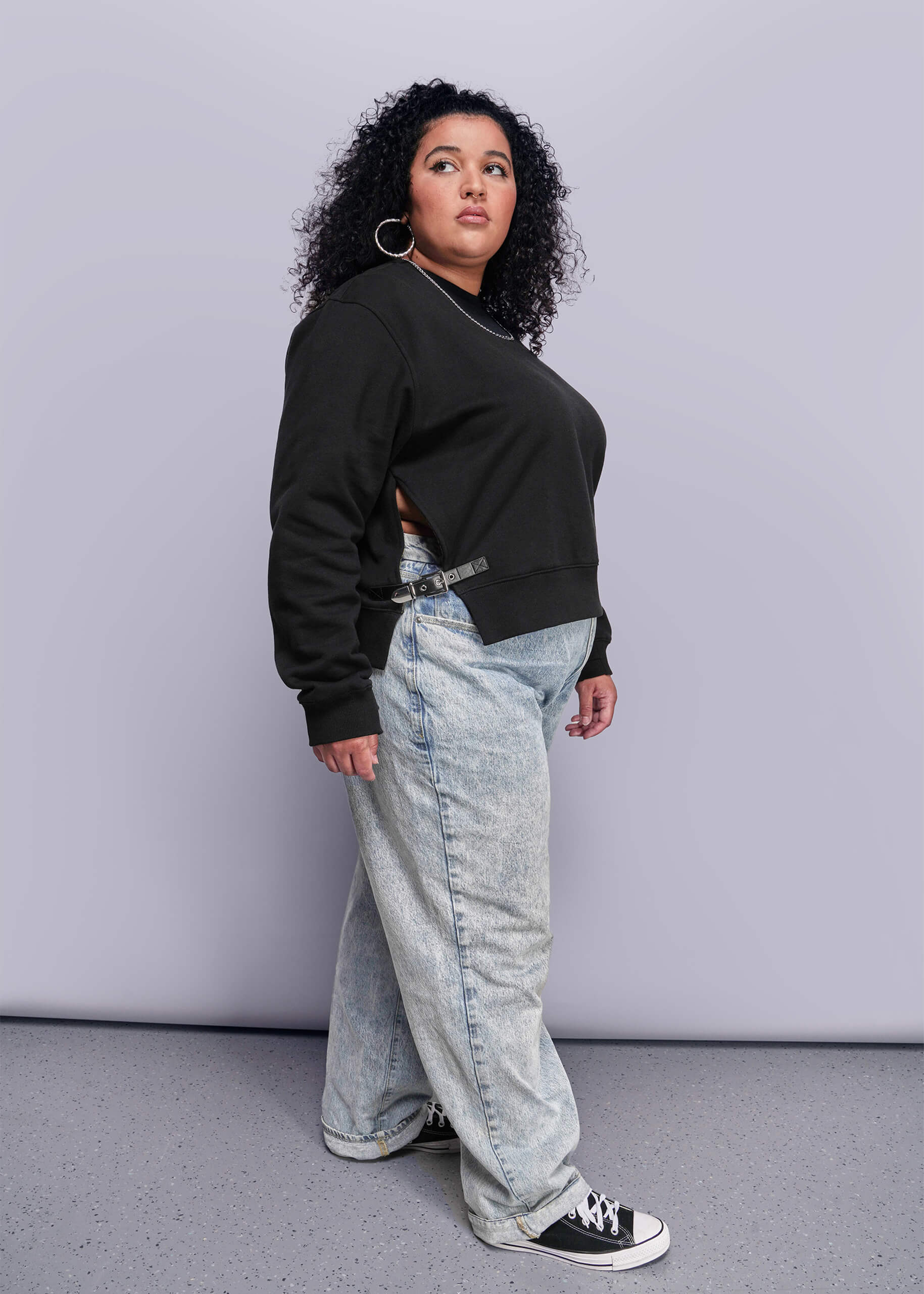 1X=Person wearing a black sweatshirt and light blue jeans against a gray background