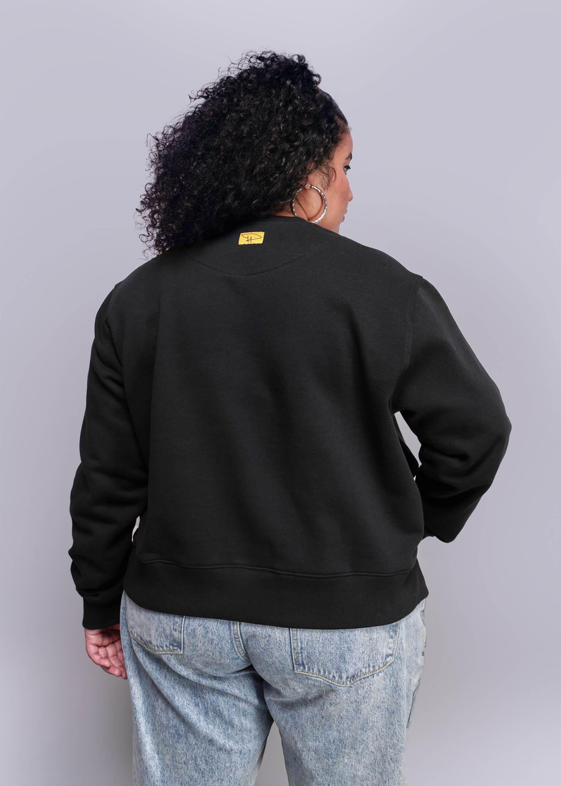 1X=Person wearing a black sweatshirt with a yellow tag on a plain background