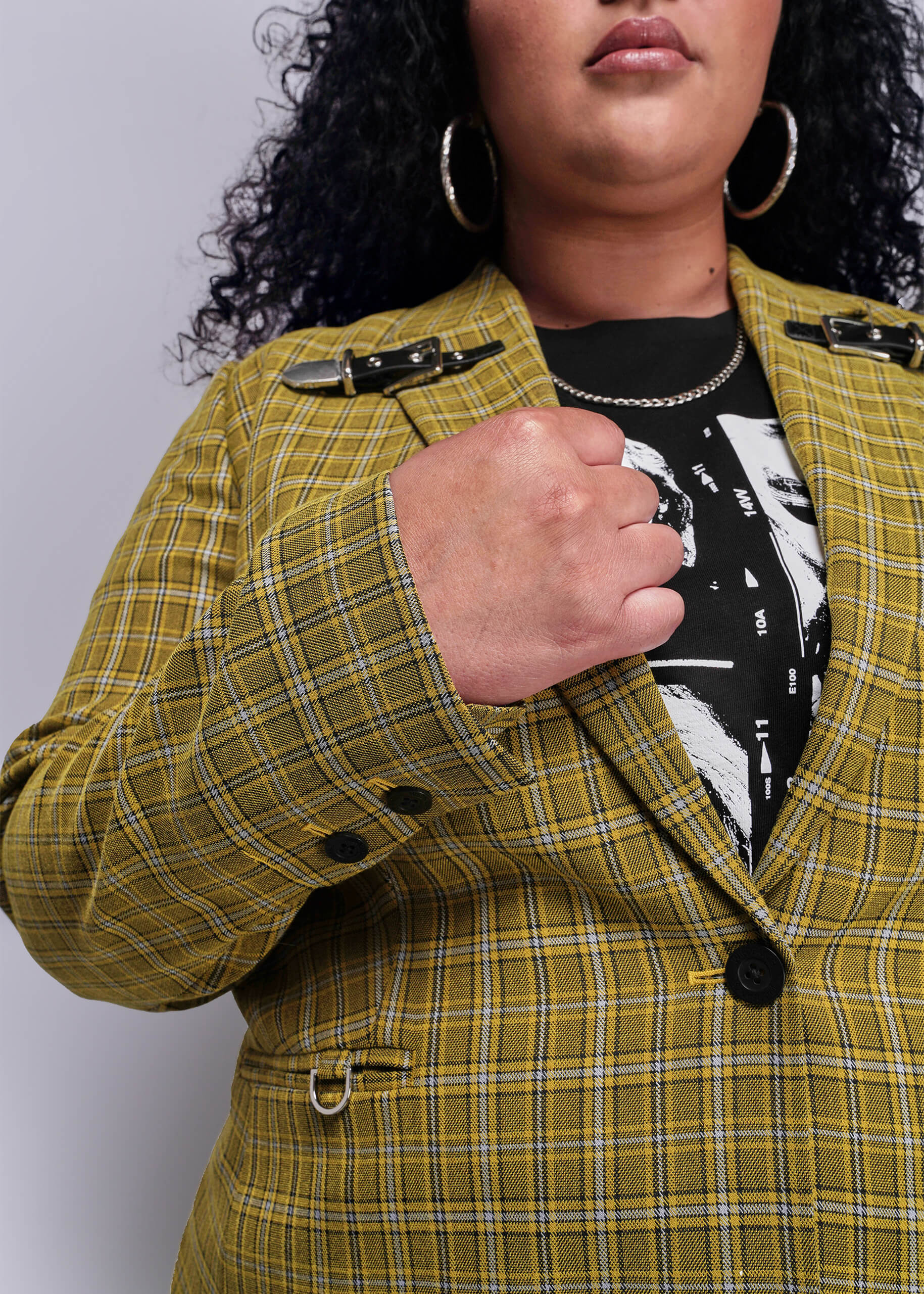1X=Close up view of person wearing a yellow plaid jacket with black buttons on a plain background