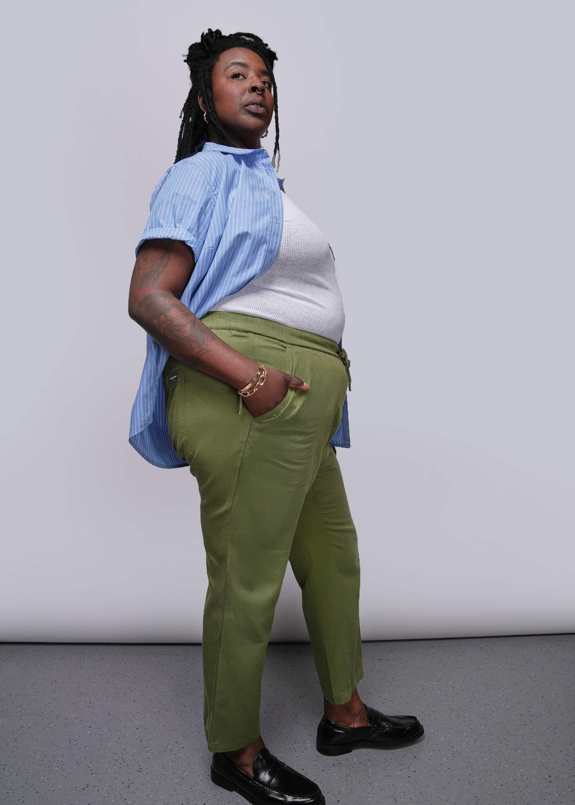 1X=Person wearing a blue shirt, white top, green pants, and black shoes against a plain background