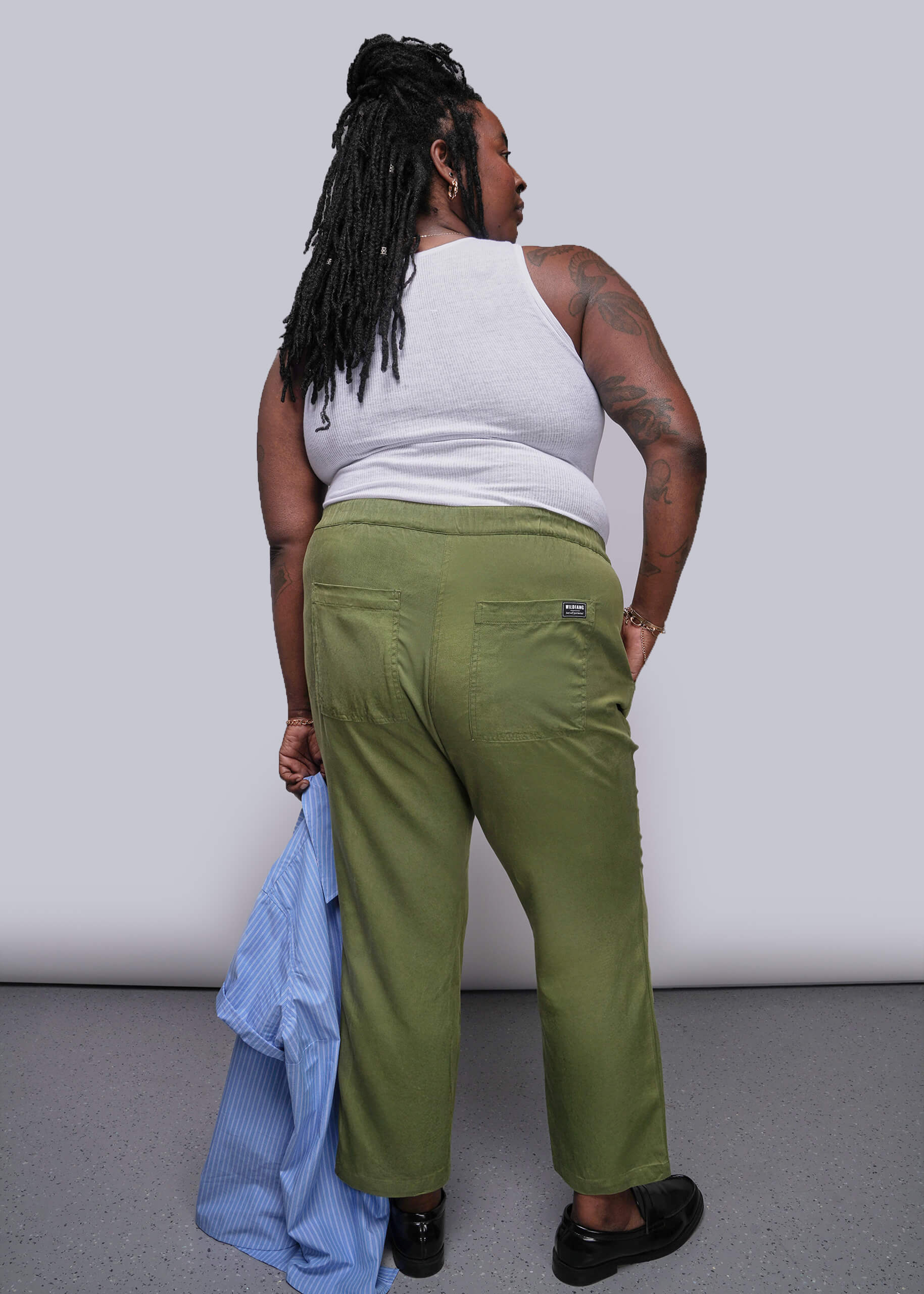 1X=Person wearing green pants and a white top against a plain background