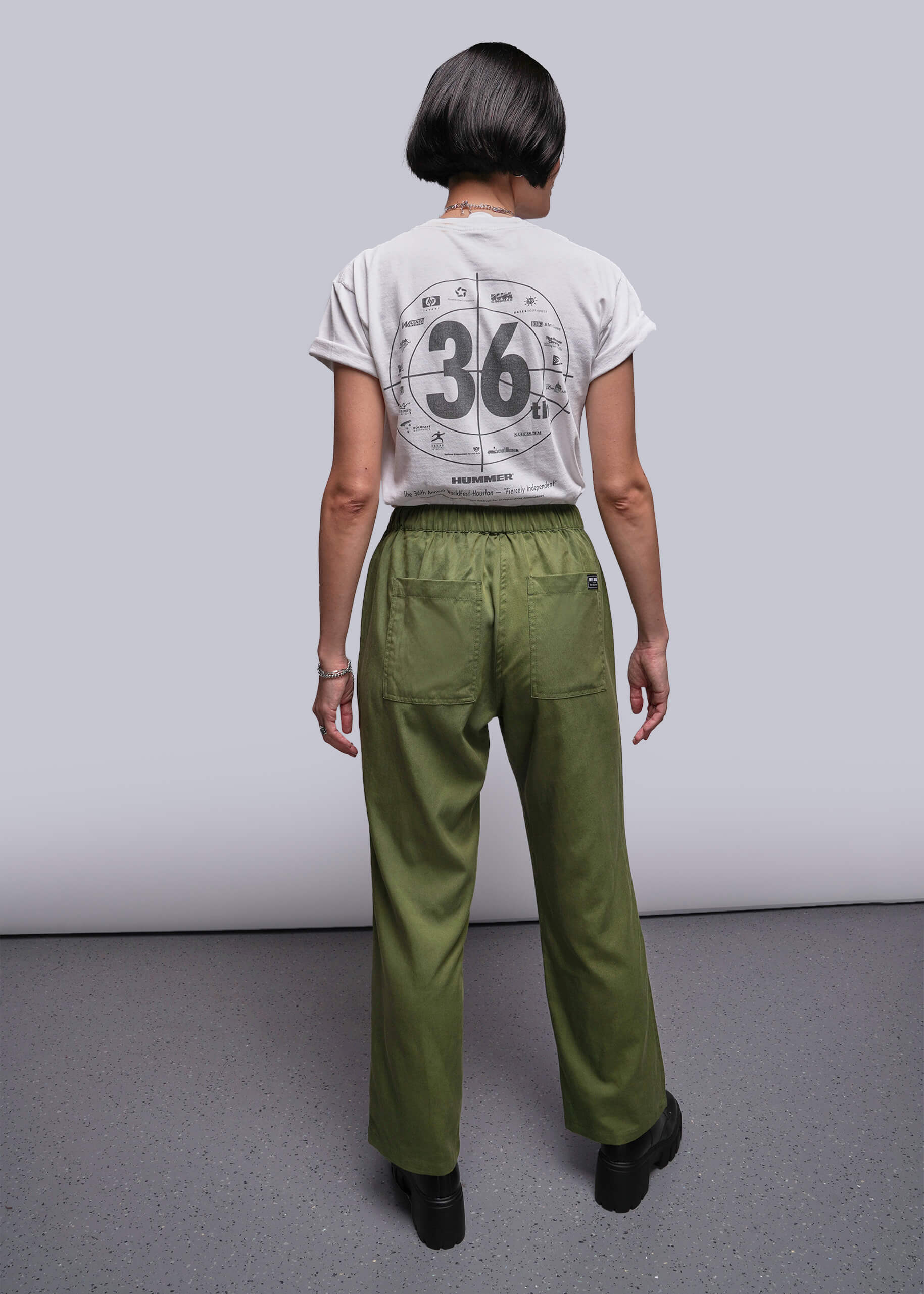 S=Person wearing a white t-shirt with a design and green pants against a plain background