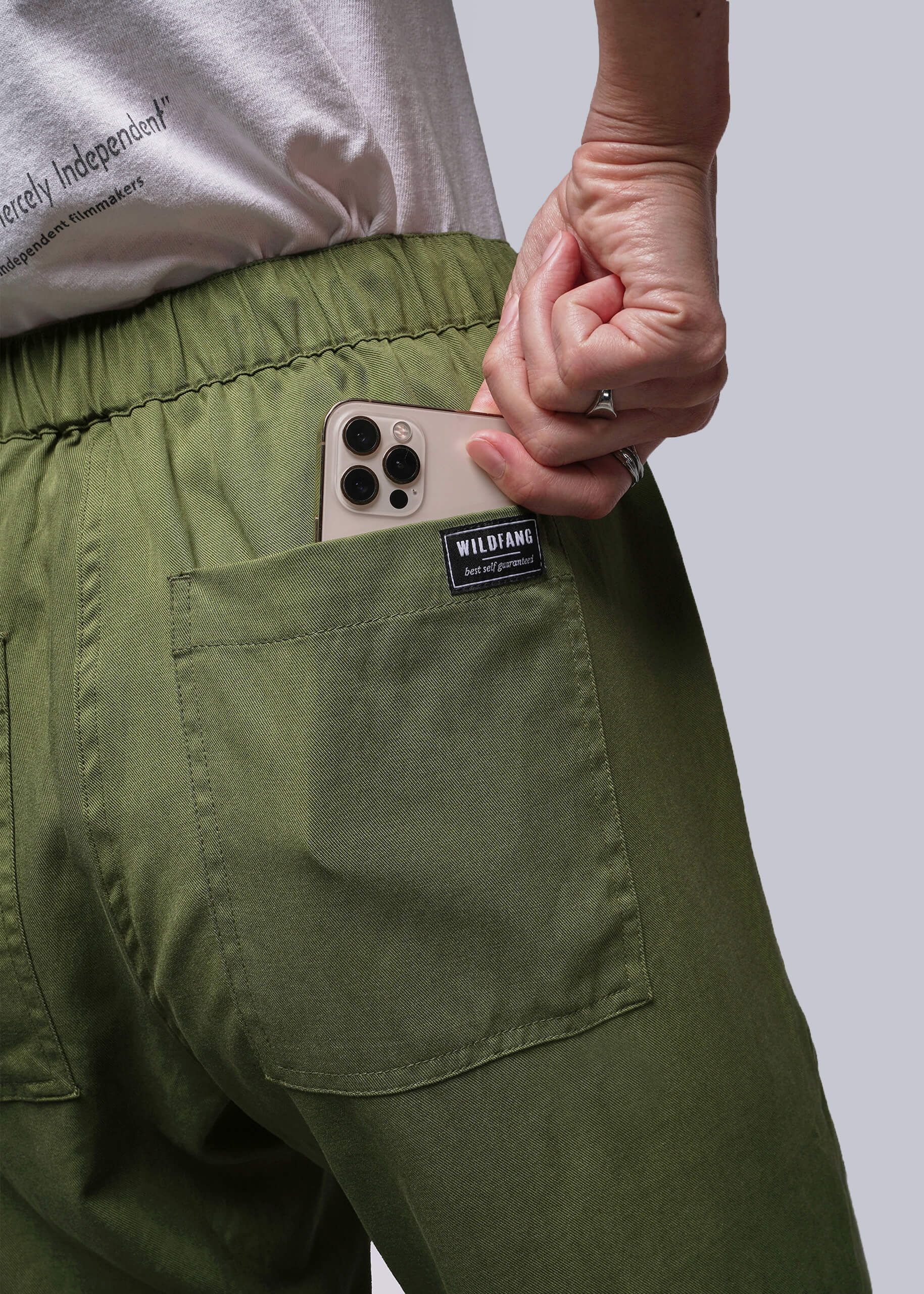 S=Person wearing green pants holding a phone with a visible brand label against a plain background
