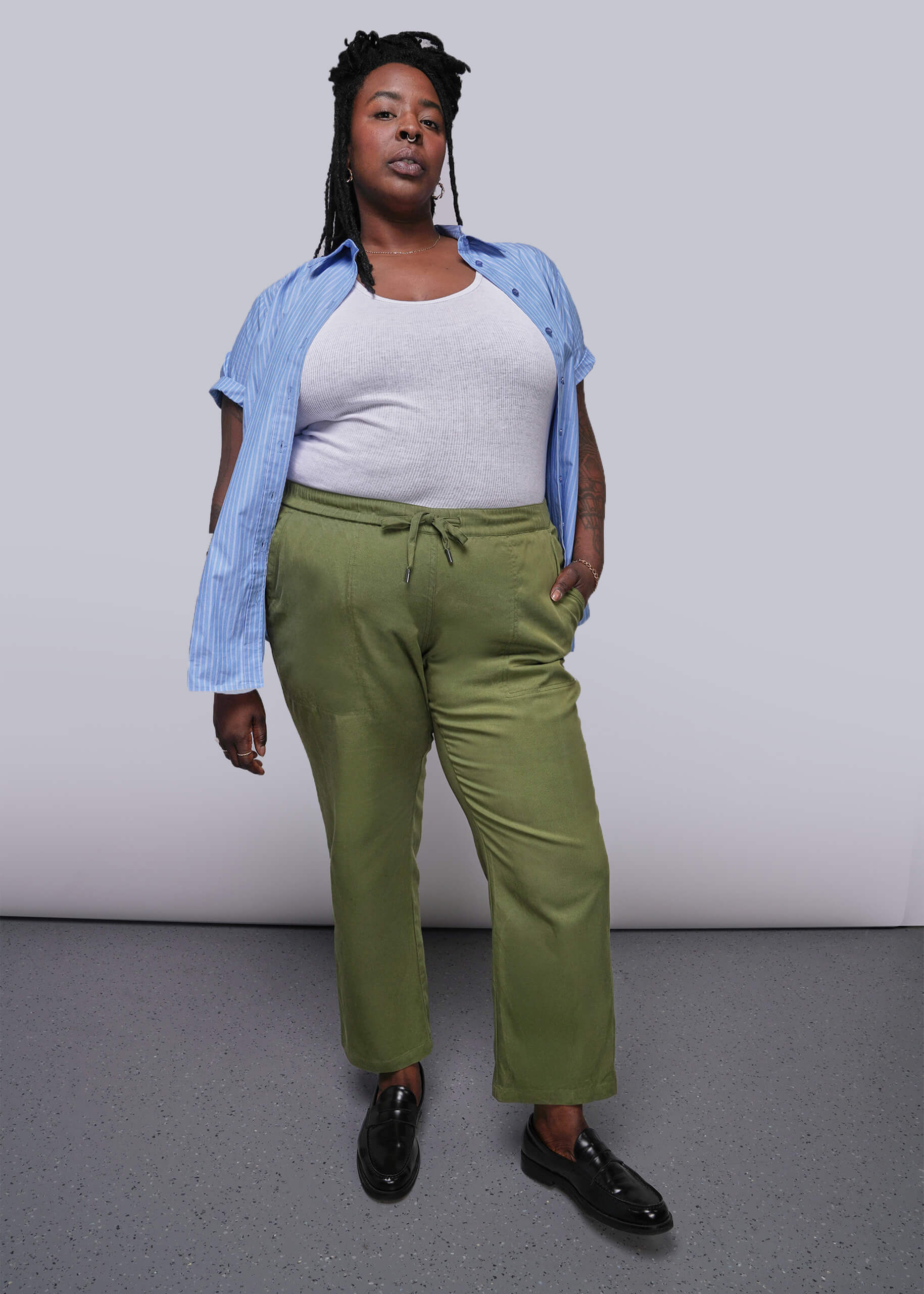1X=Person wearing a white top, blue shirt, green pants, and black shoes on a plain background
