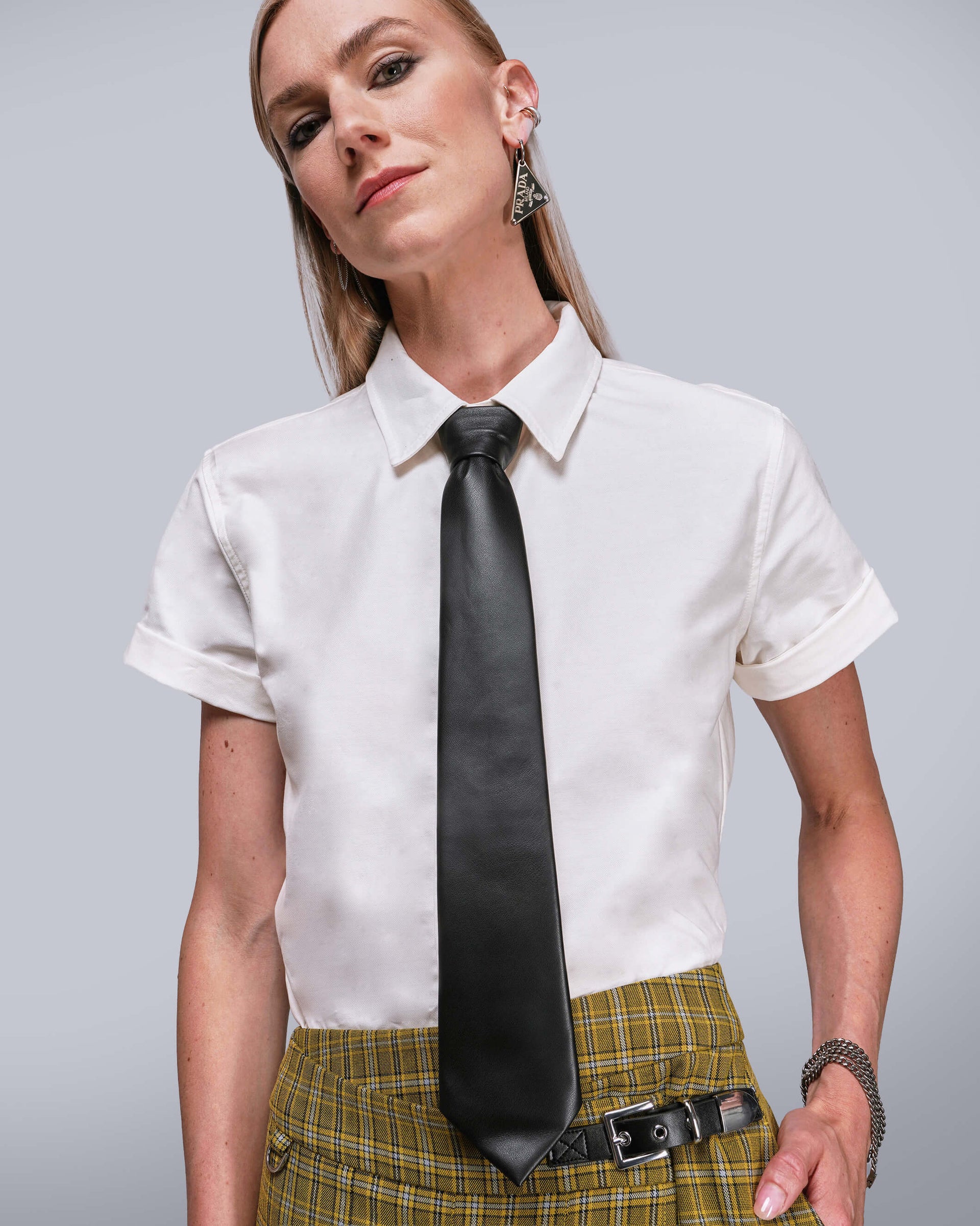 Person wearing a white shirt with a long black tie and plaid skirt on a gray background
