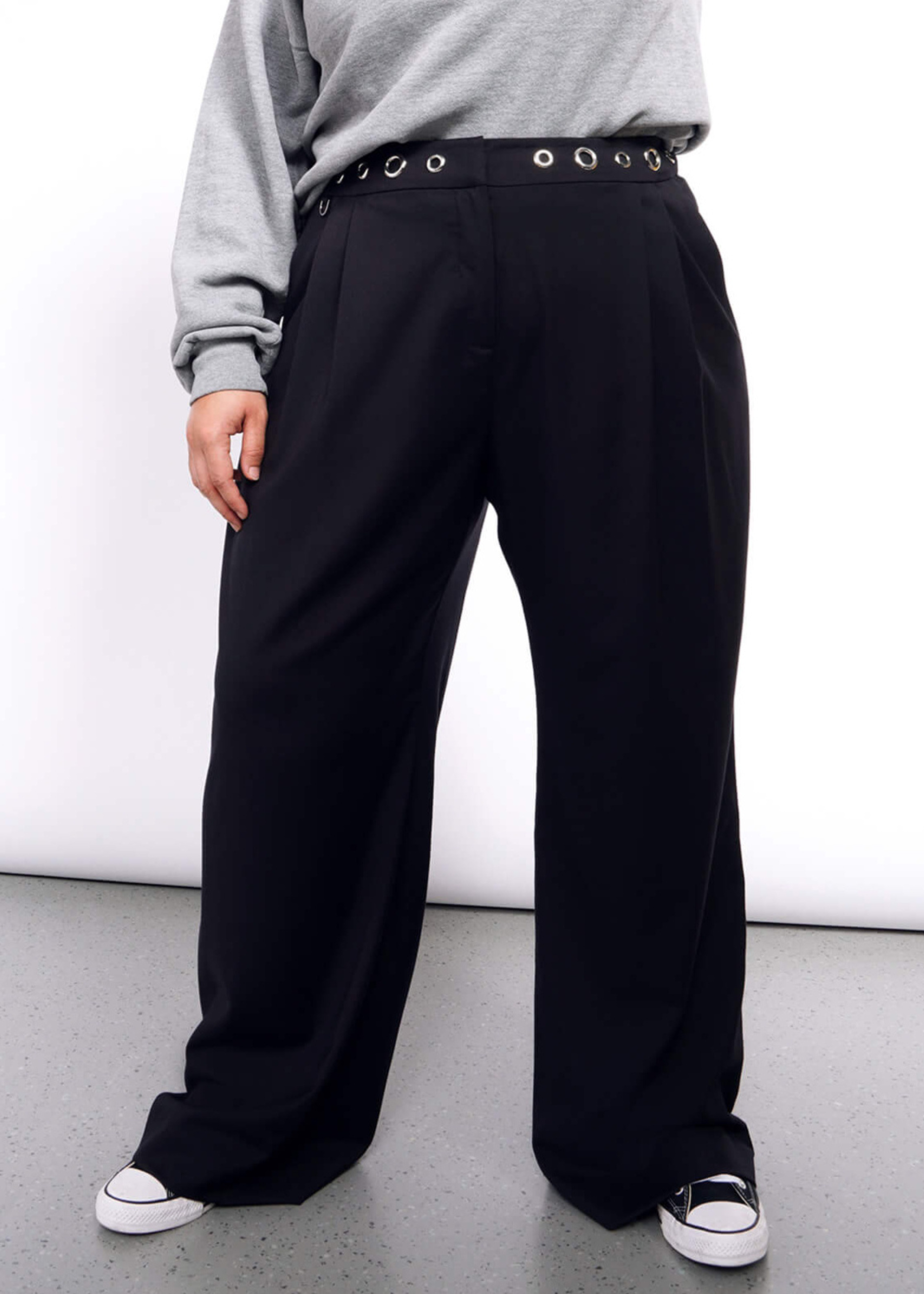 Pictured from chest down, model wears grey sweater and black wide leg trouser with grommet waist detail.